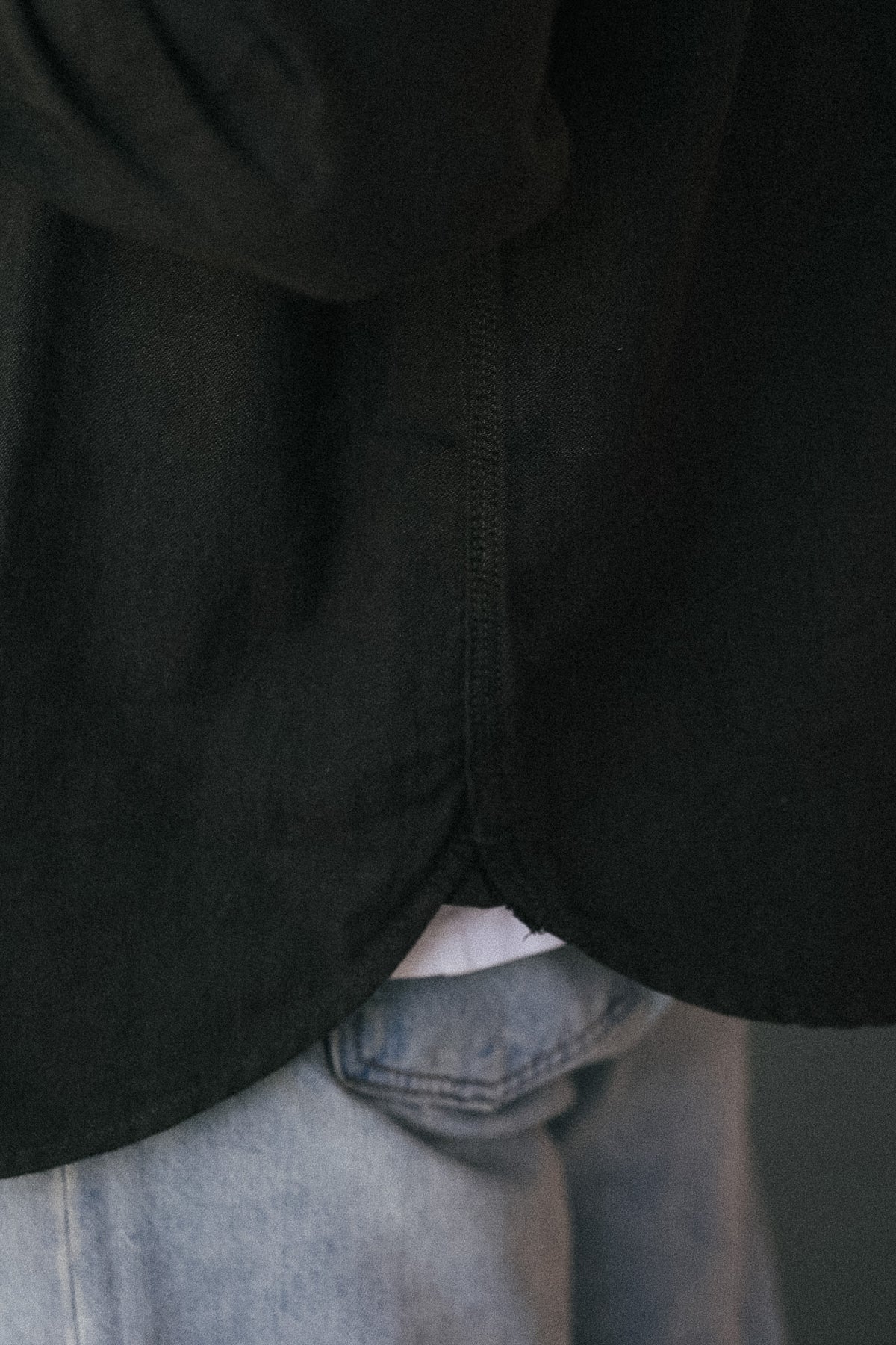 Close-up of a person wearing a black long-sleeve top or jacket over a white undershirt, paired with light blue jeans.