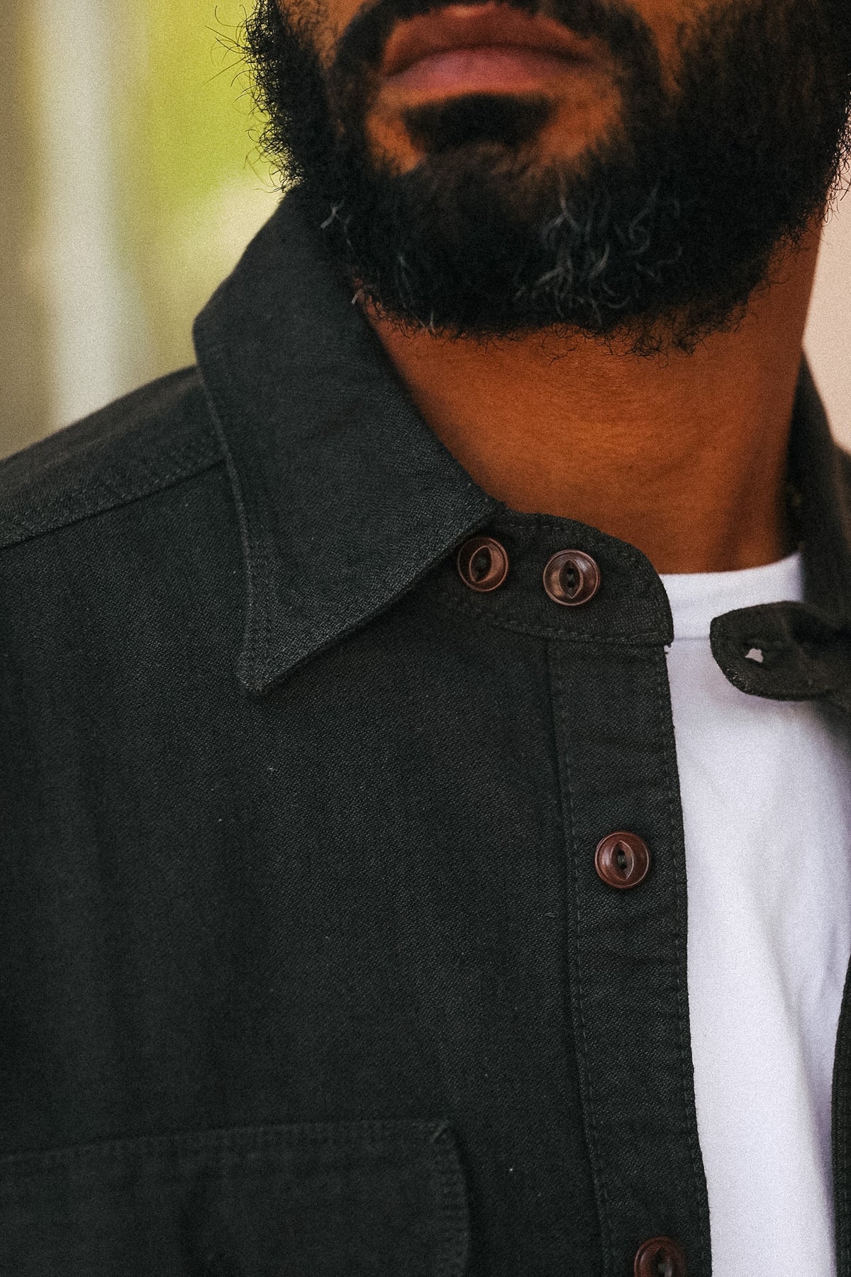 Close-up of a man wearing a dark charcoal gray button-down shirt over a white t-shirt, showing the collar, brown buttons, and beard.