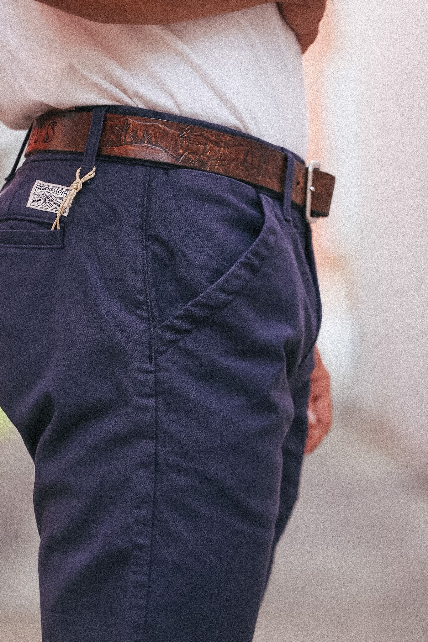 Navy pants with a brown belt and visible brand logo on a blurred background