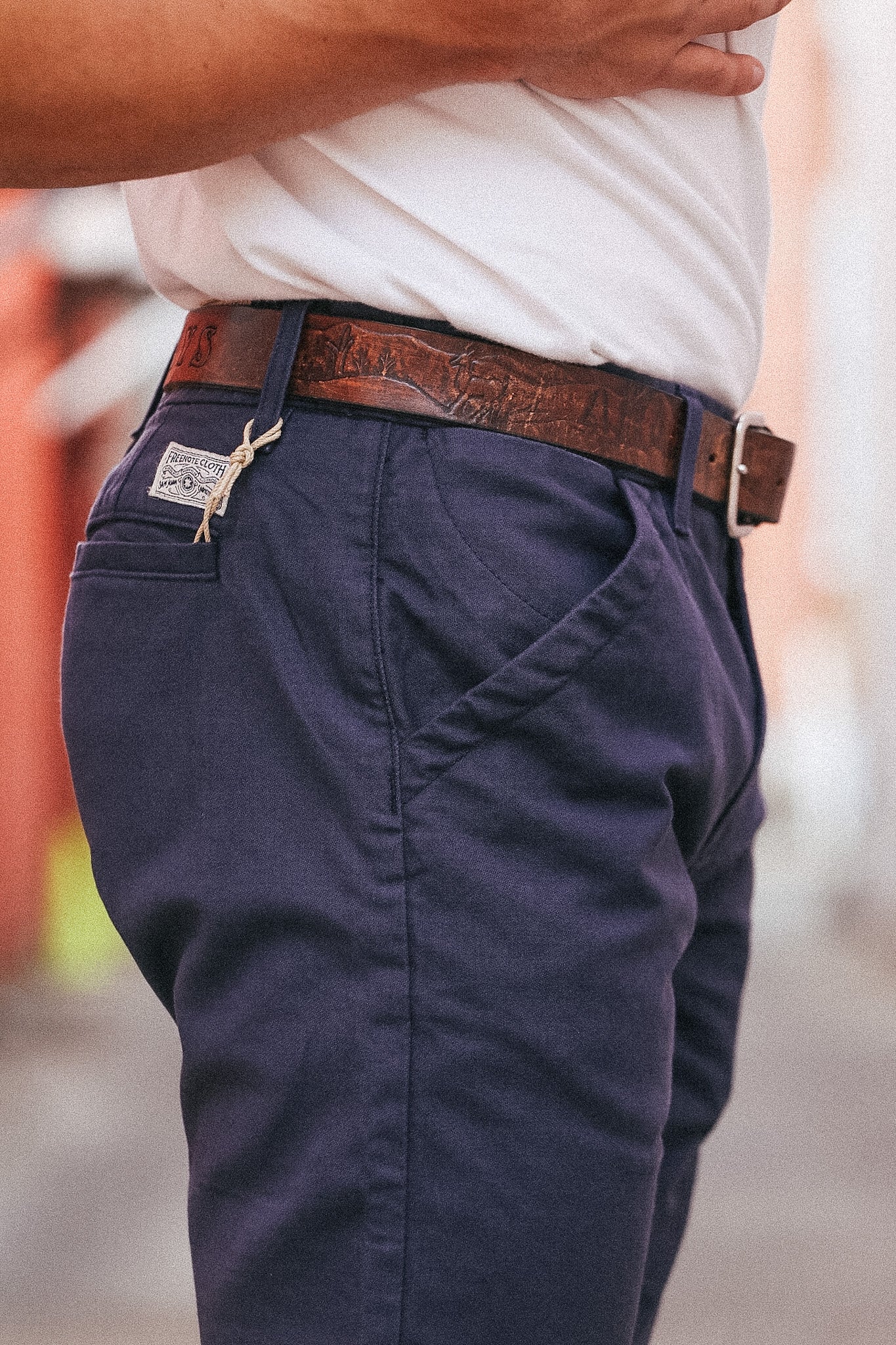 Navy blue pants with a brown belt worn by a person, blurred background