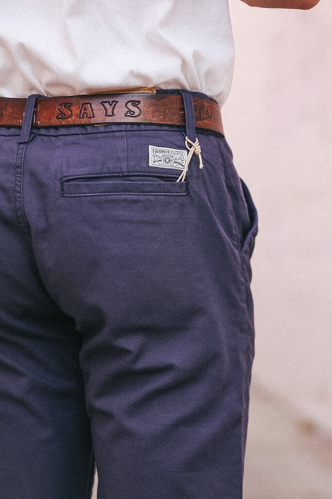 Navy pants with a brown belt and 'SAYS' logo on a light background