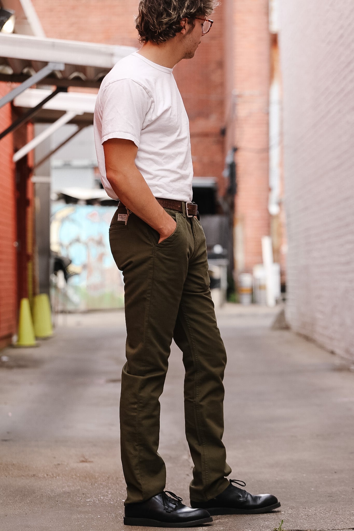 Man wearing a white t-shirt and green pants standing on a sidewalk.
