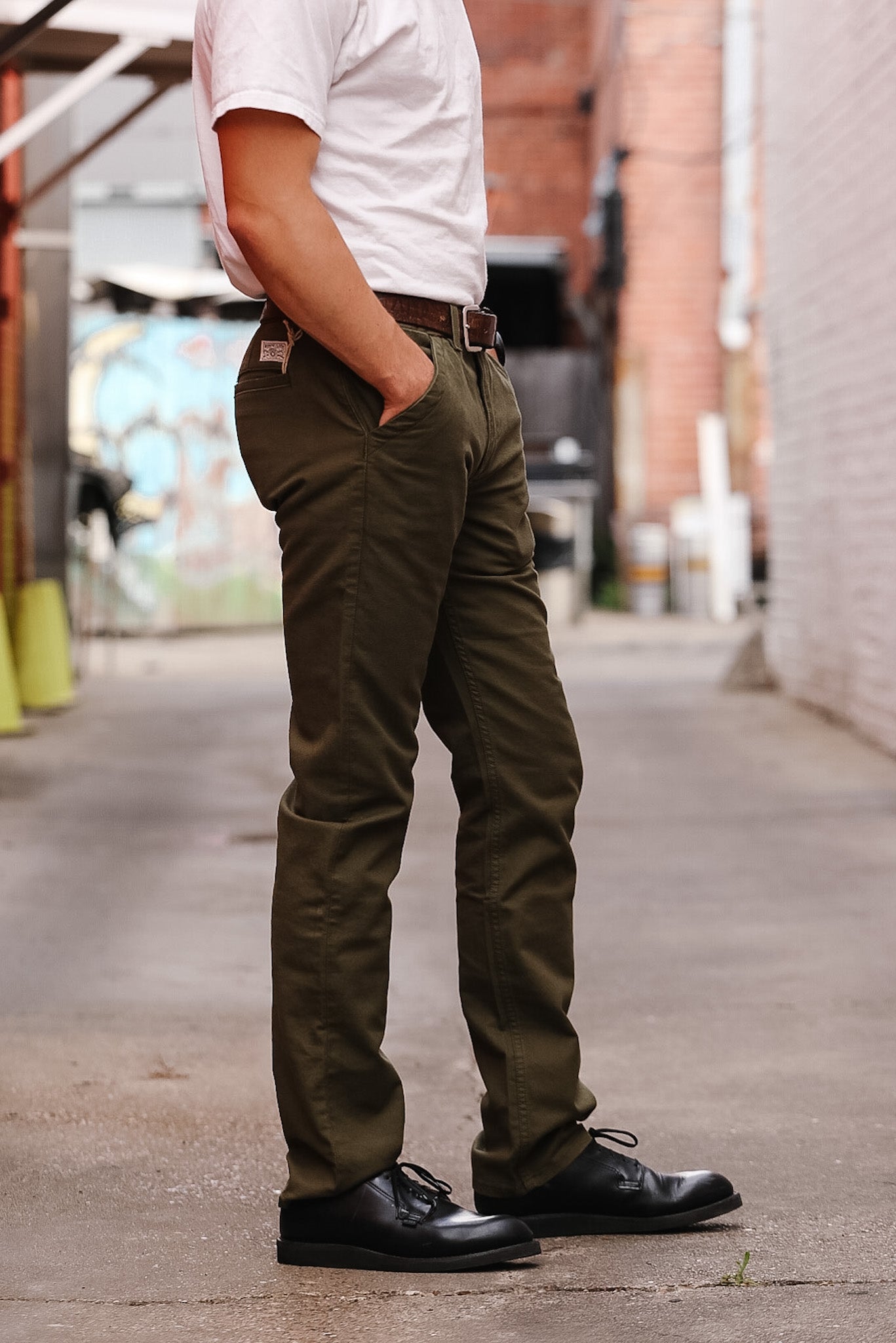 Person wearing olive green pants and black shoes on a sidewalk.