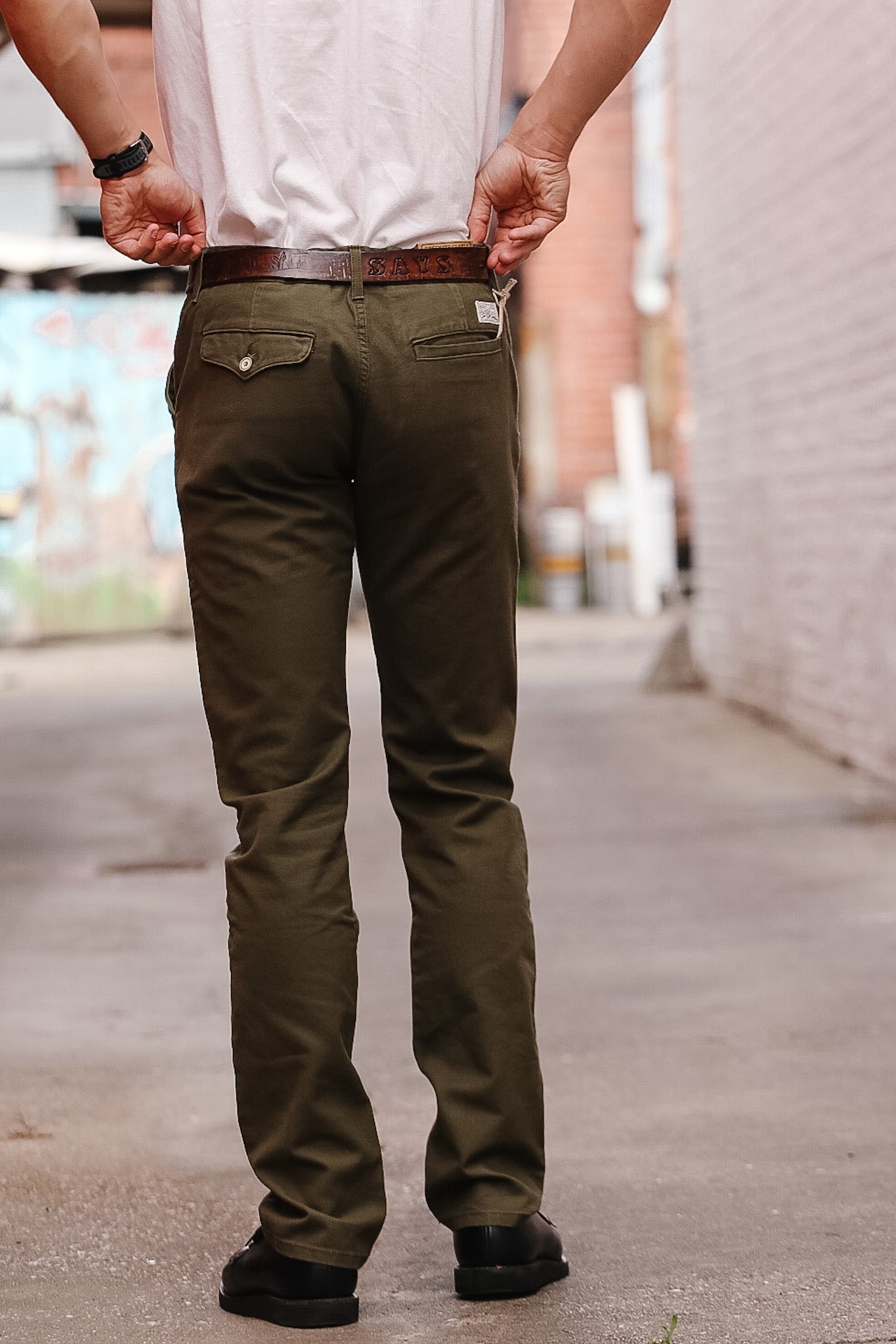 Person wearing olive green pants and a white shirt on a blurred street background