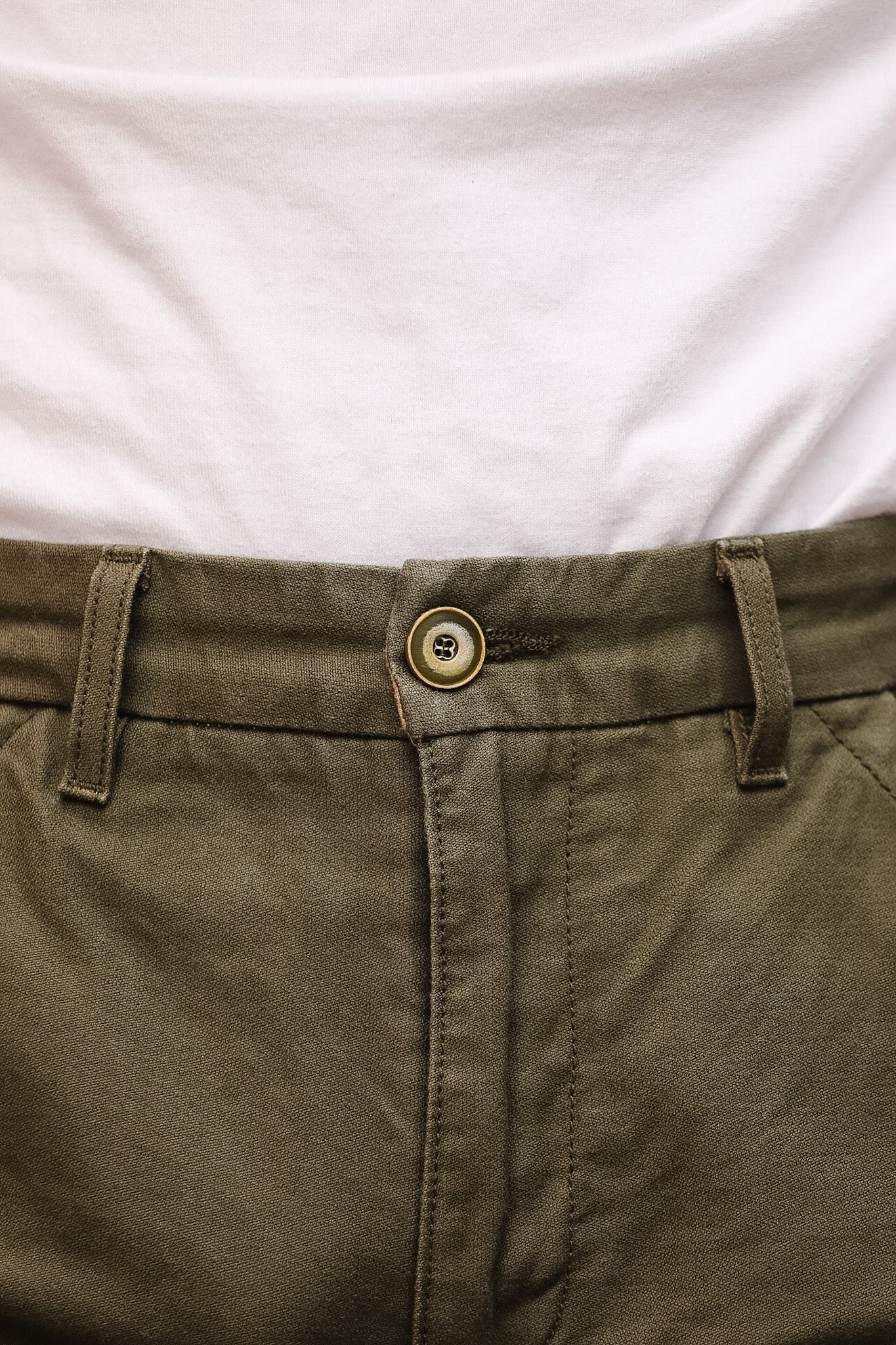 Close-up of a button on brown pants with a white shirt background