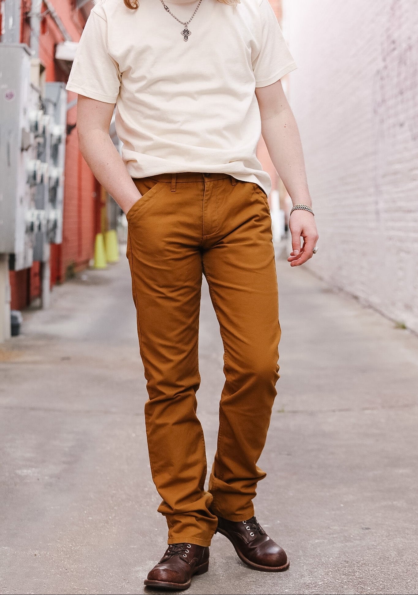 Person wearing a white t-shirt and brown pants standing on a street.