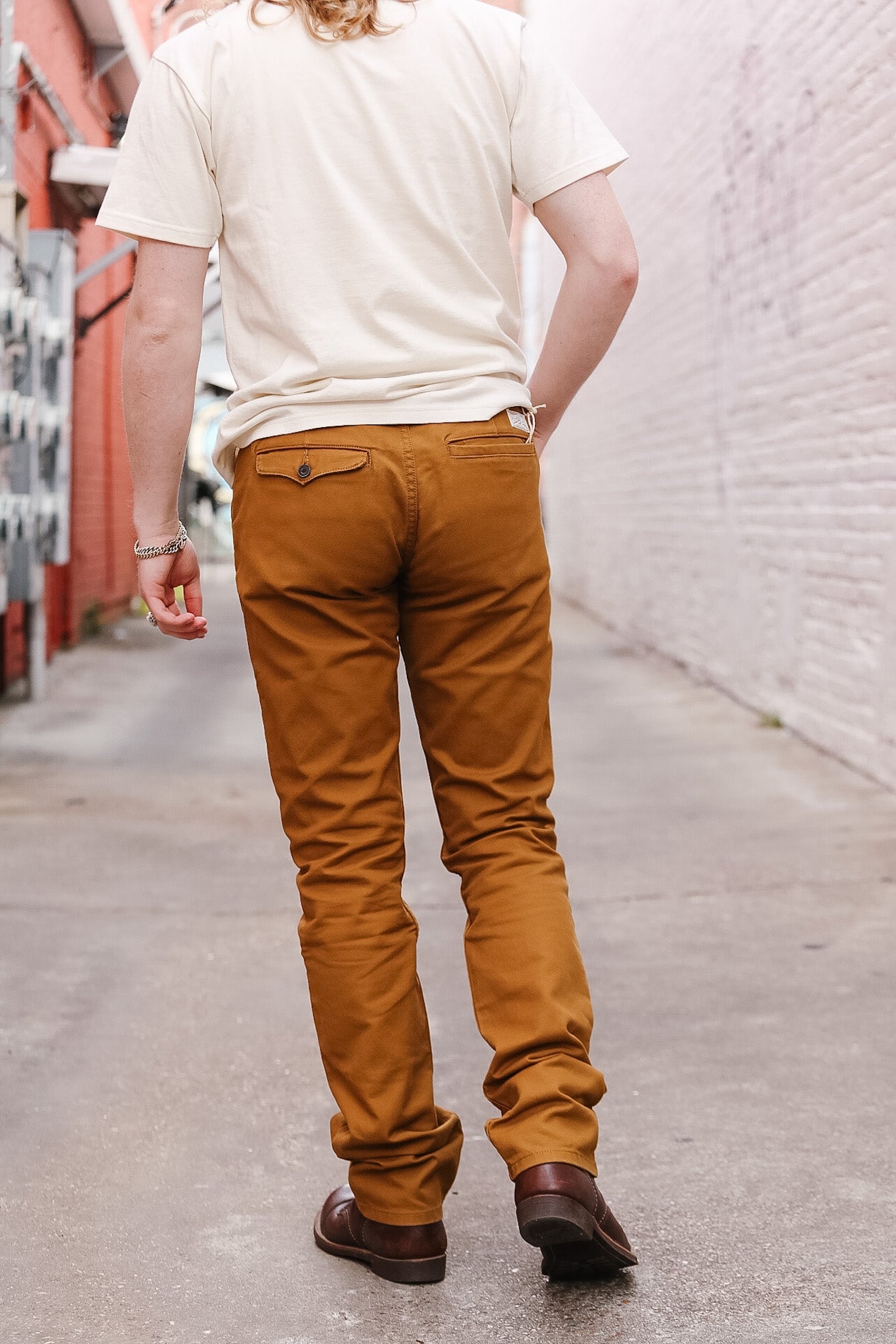 Person wearing mustard yellow pants and a white shirt walking down a street.