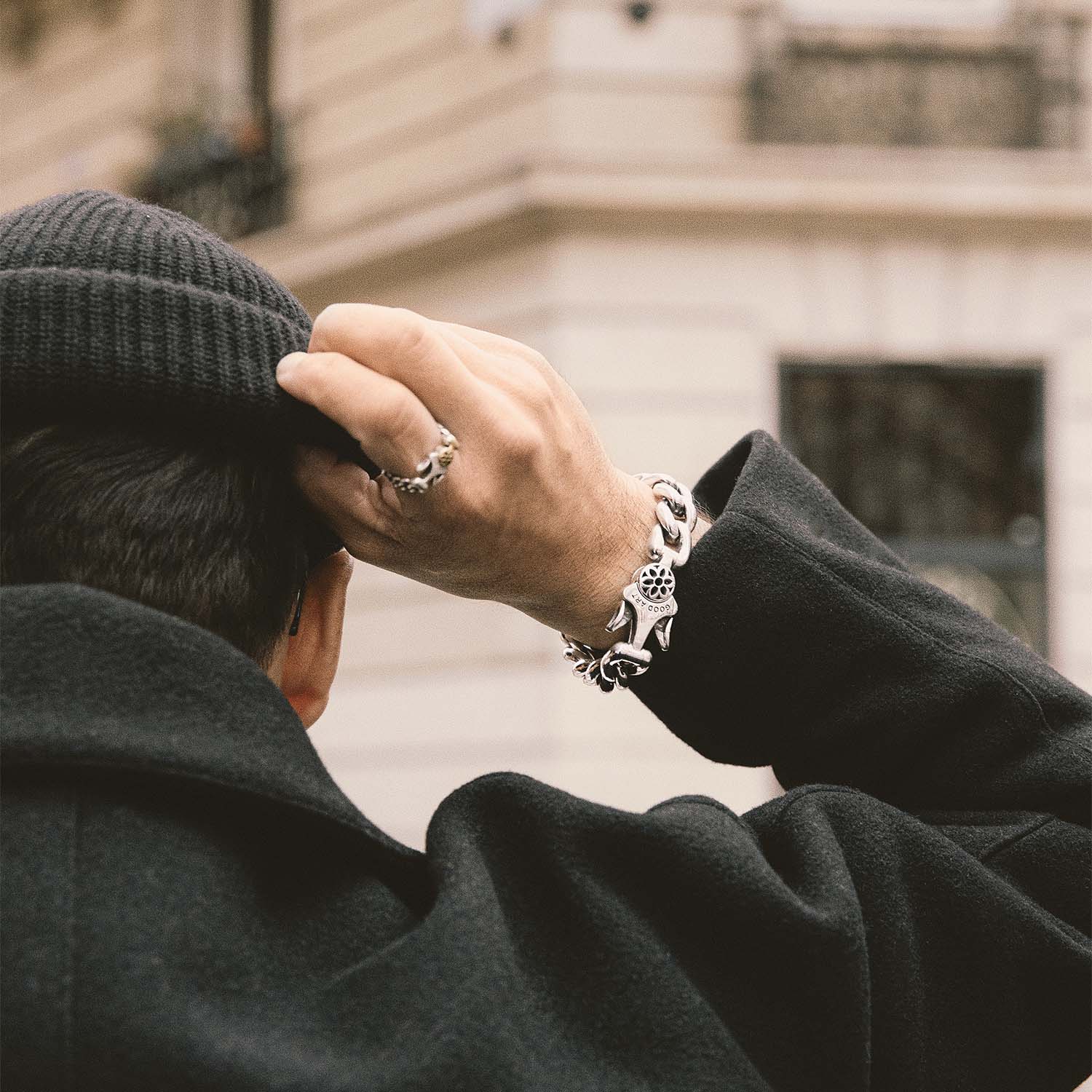 Man wearing black knit beanie and coat, showcasing silver chain bracelet and skull ring