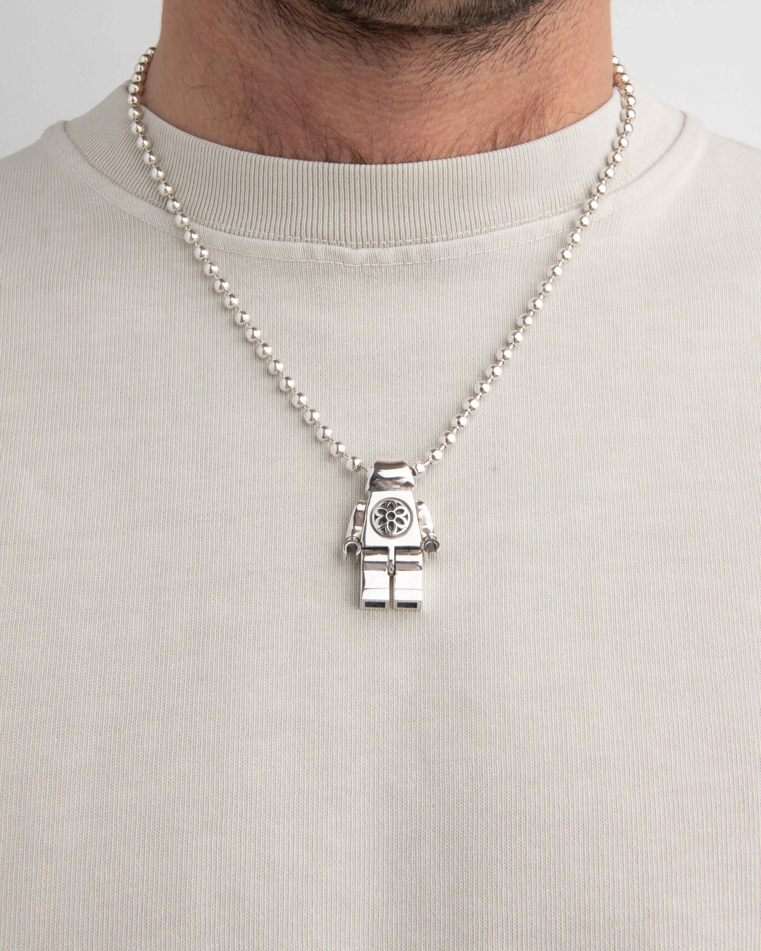 Sterling silver robot pendant necklace with detailed torso on ball chain worn over beige shirt