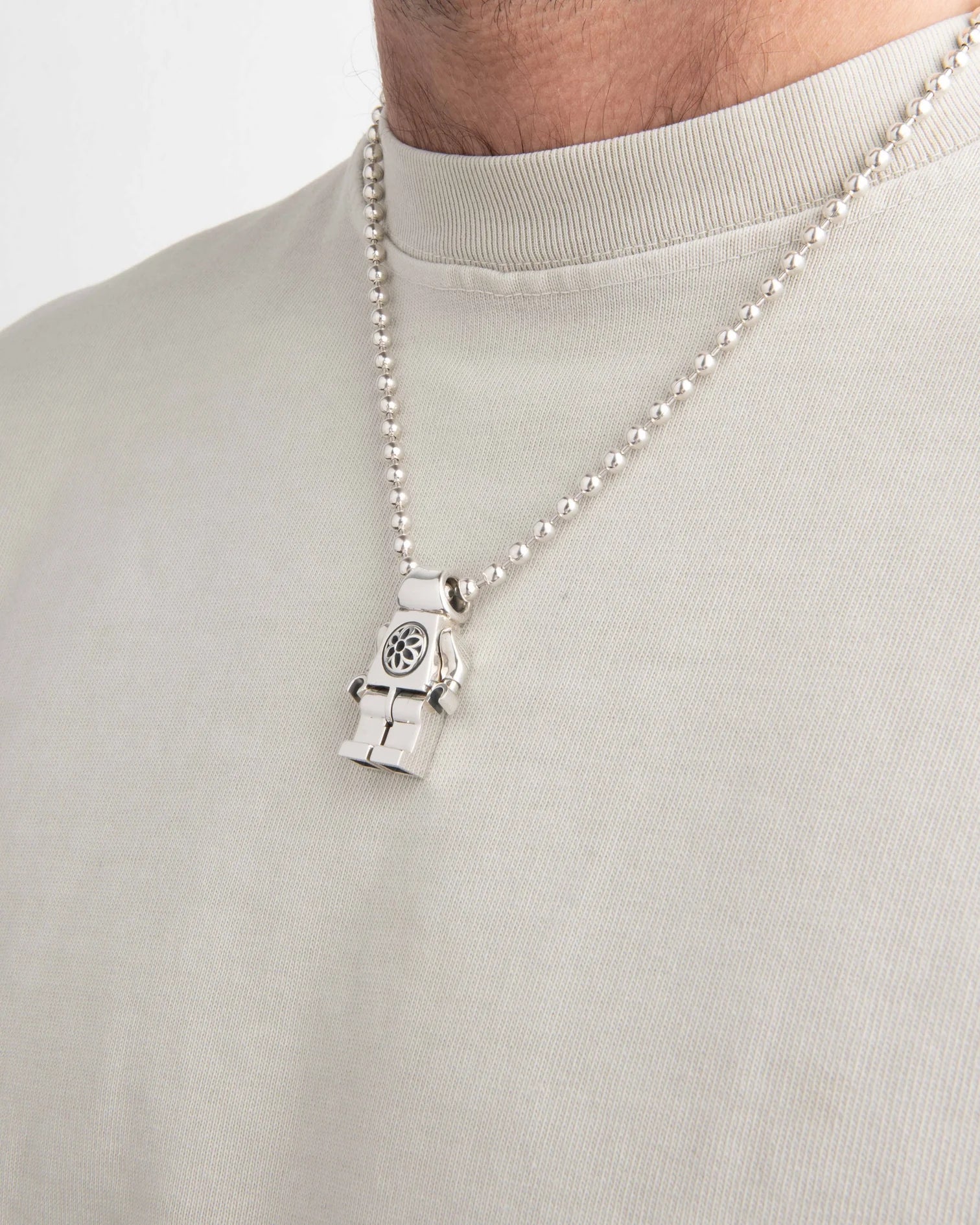 Sterling silver figure pendant on a ball chain necklace worn with a light beige shirt