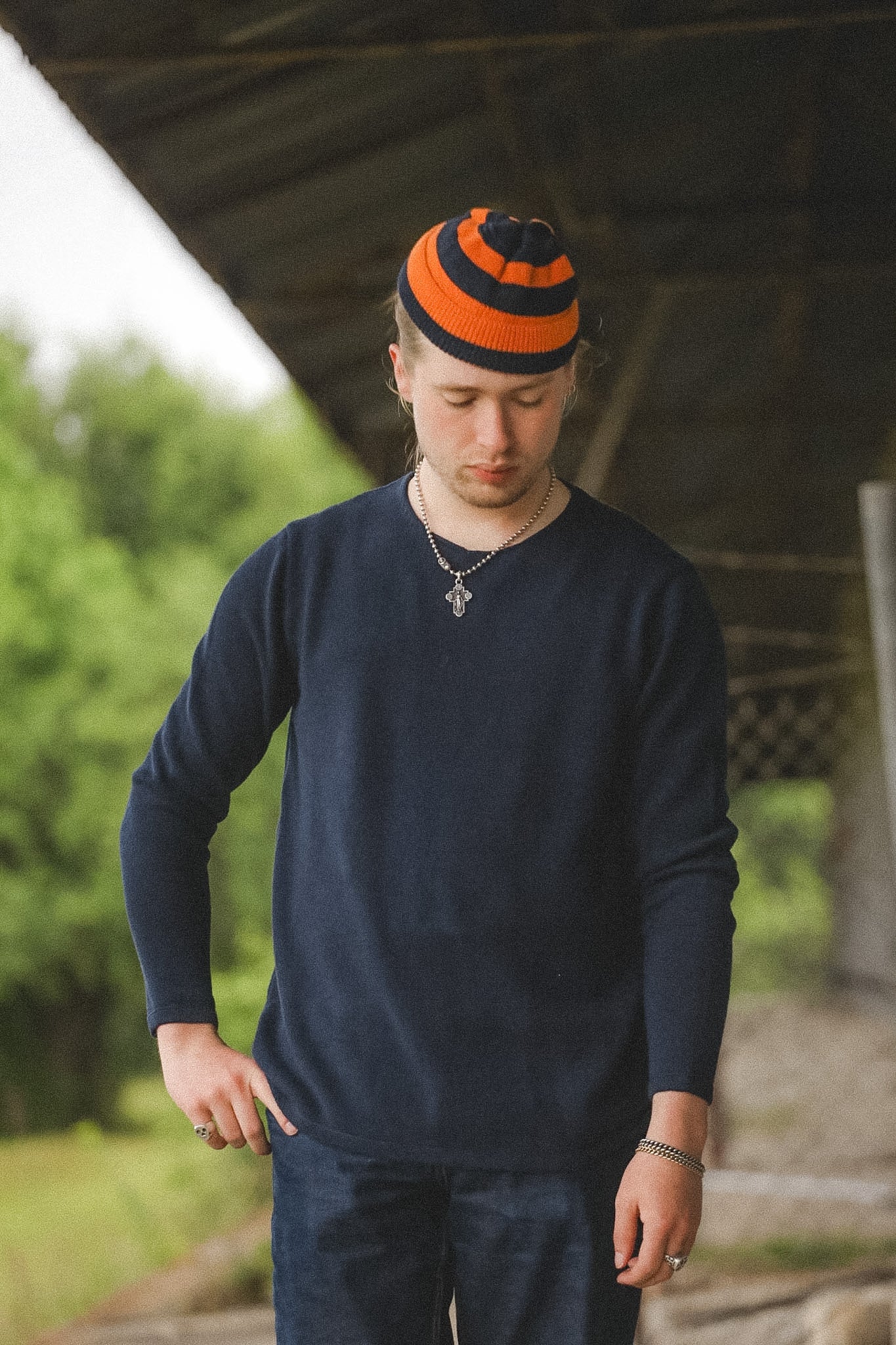 Man wearing a dark blue sweater and orange and black beanie standing outdoors.