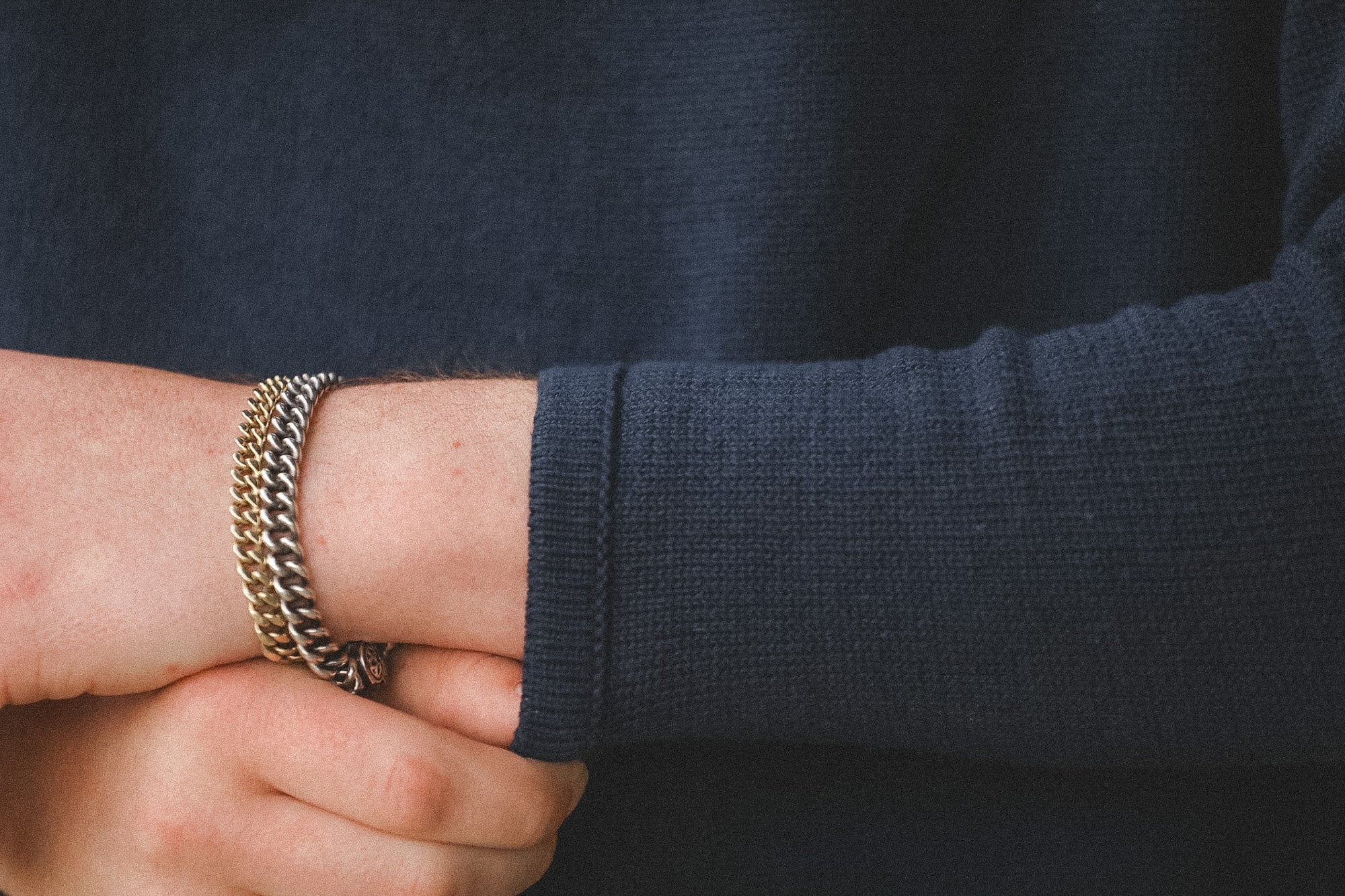 Close-up of a person wearing a gold chain bracelet on a dark sleeve.