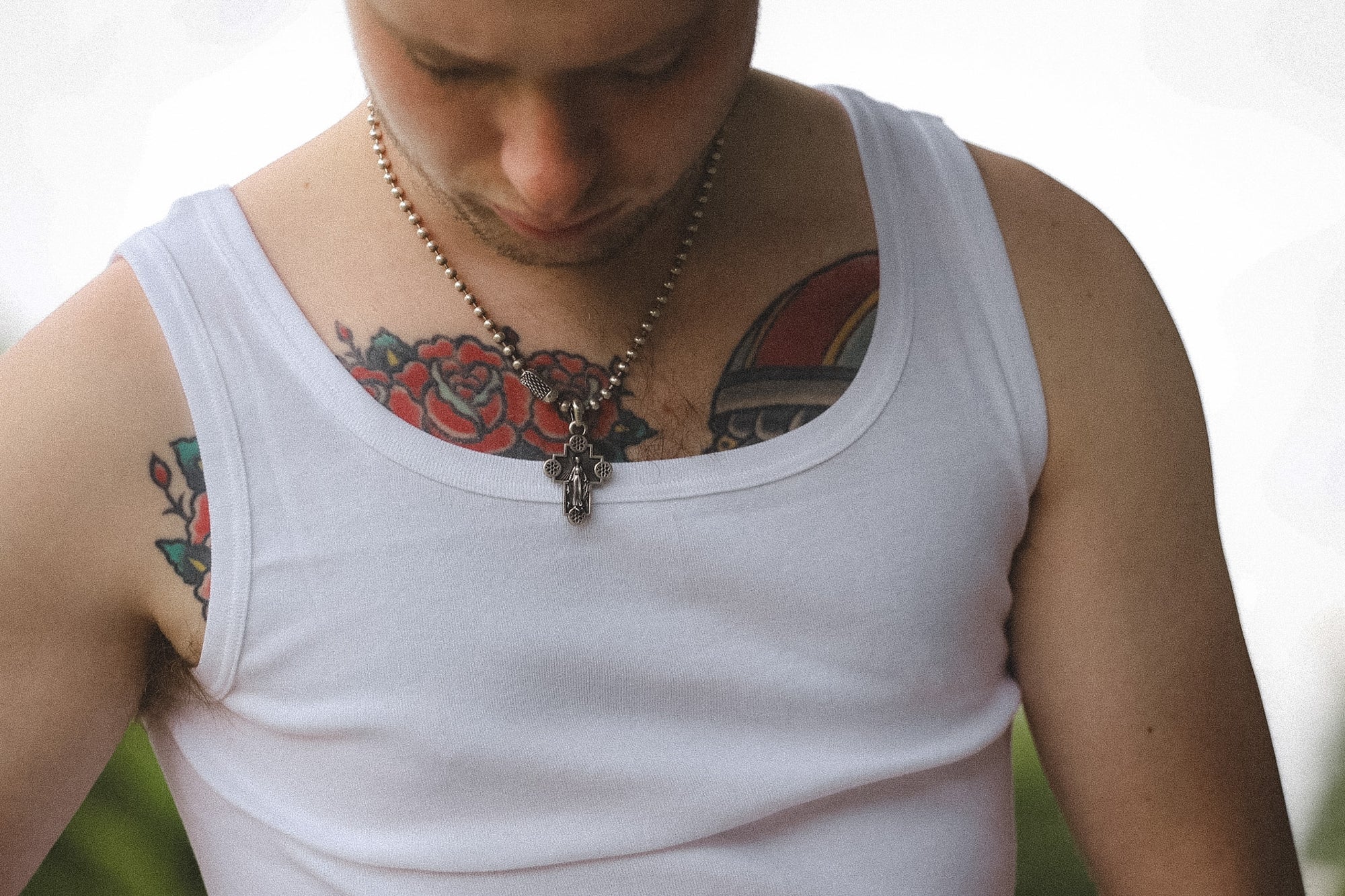 Person wearing a white tank top with visible tattoos on a blurred background