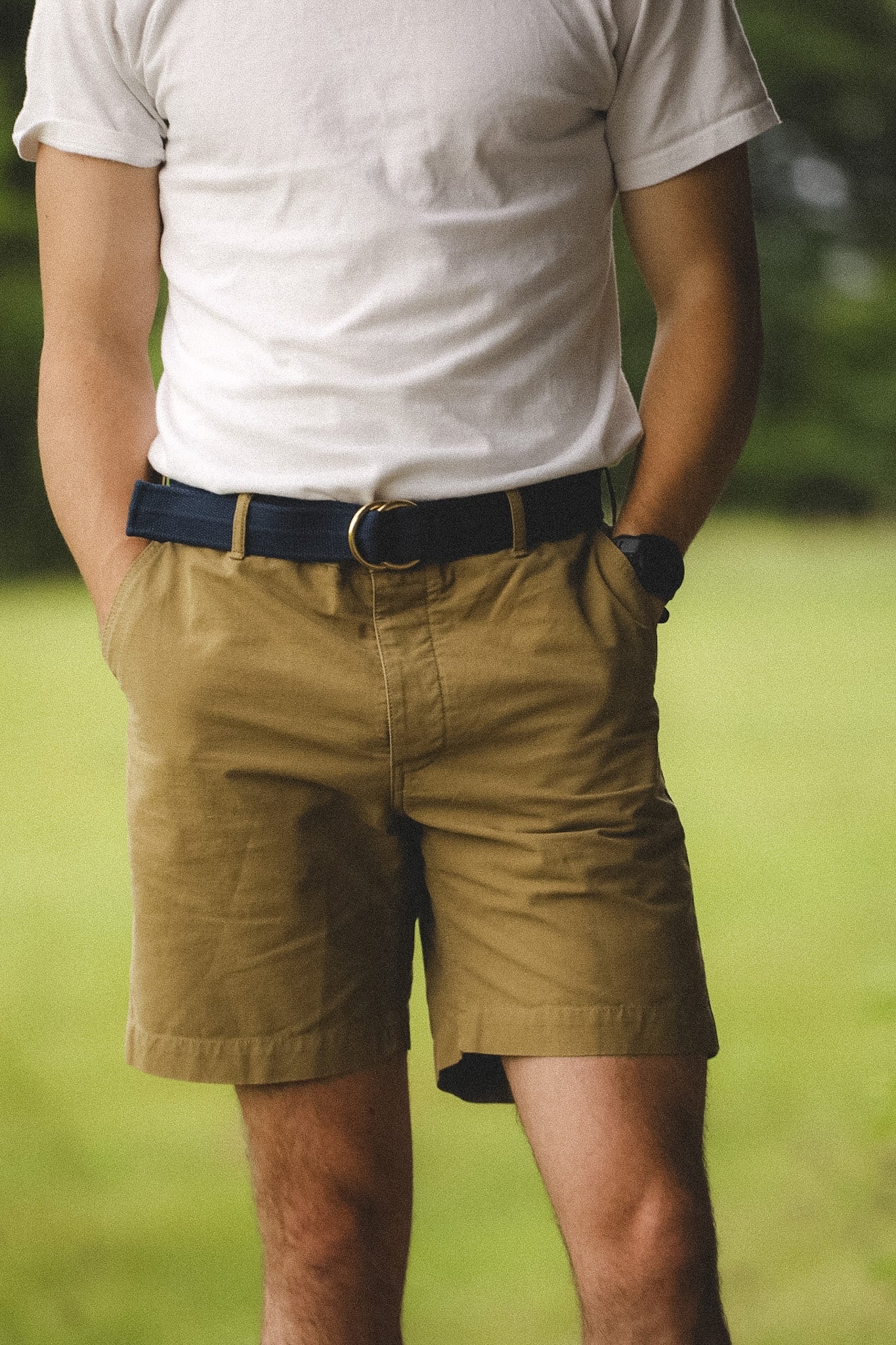 Person wearing a white t-shirt and beige shorts with a blurred green background