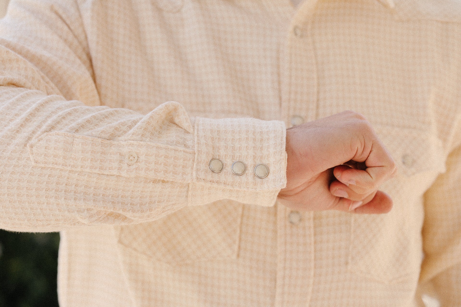 Close-up of a cream houndstooth flannel shirt cuff with metal snap buttons, worn by a person