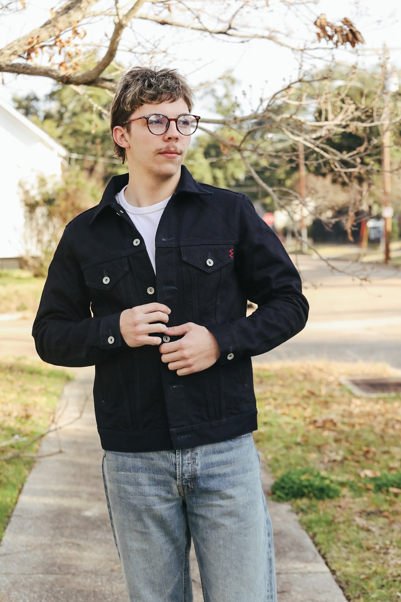 Person wearing a black jacket and glasses outdoors on a sidewalk.