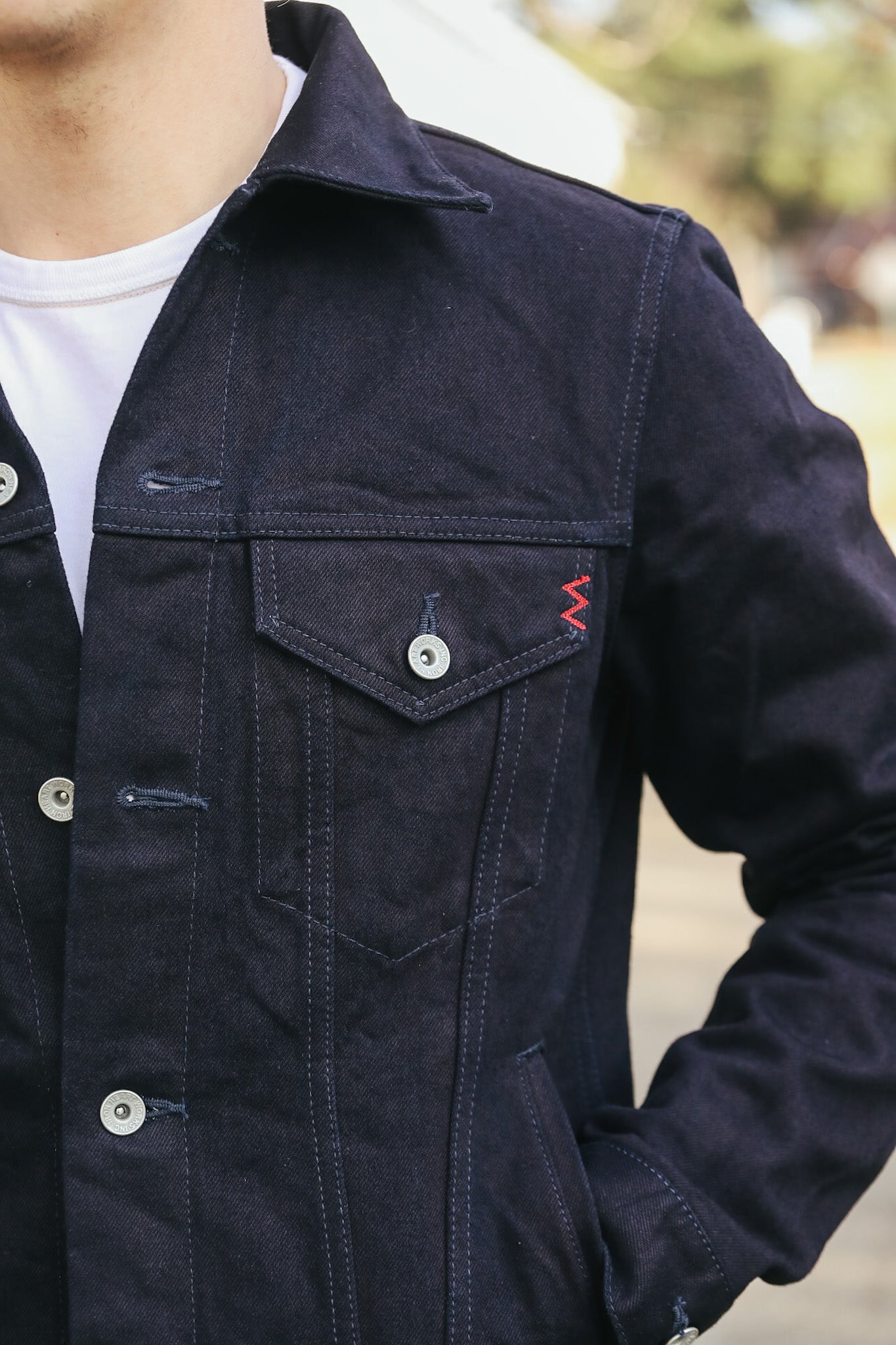 Navy blue jacket with a red logo on the chest pocket, worn by a person.