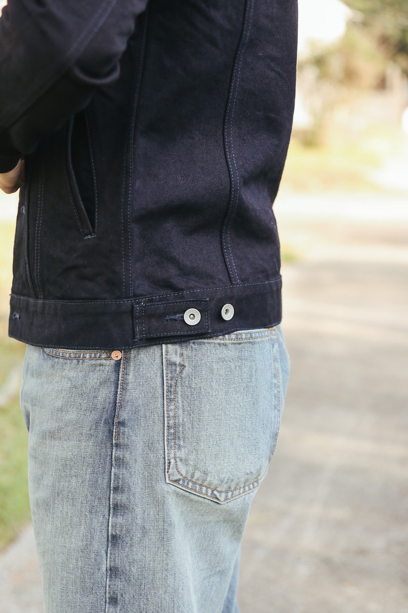 Person wearing a dark jacket and light blue jeans outdoors