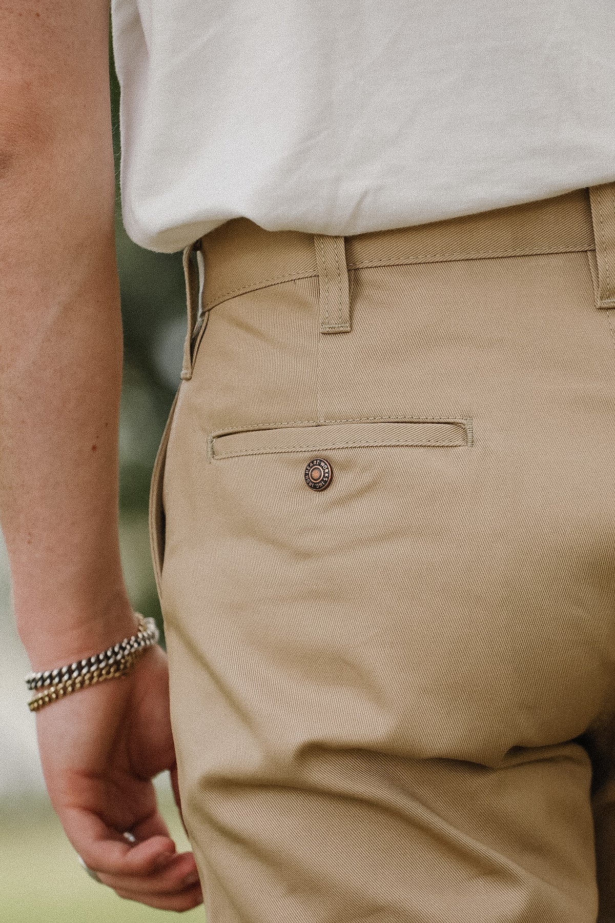 Close-up of a person wearing khaki chino pants with a white shirt, showing the back pocket and button detail.