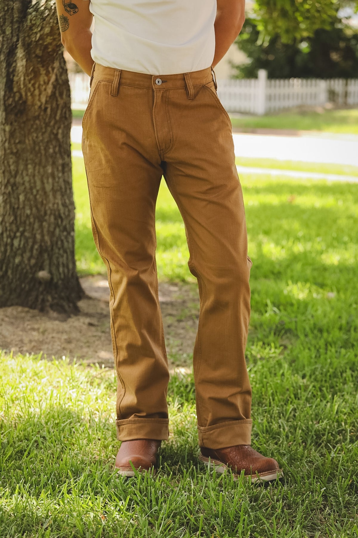 Person wearing brown pants standing on grass next to a tree