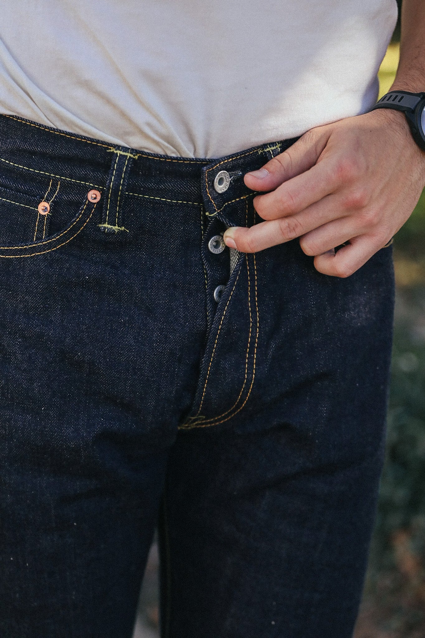 Close-up of person wearing dark selvedge denim jeans with button fly and yellow stitching from Iron Shop Provisions