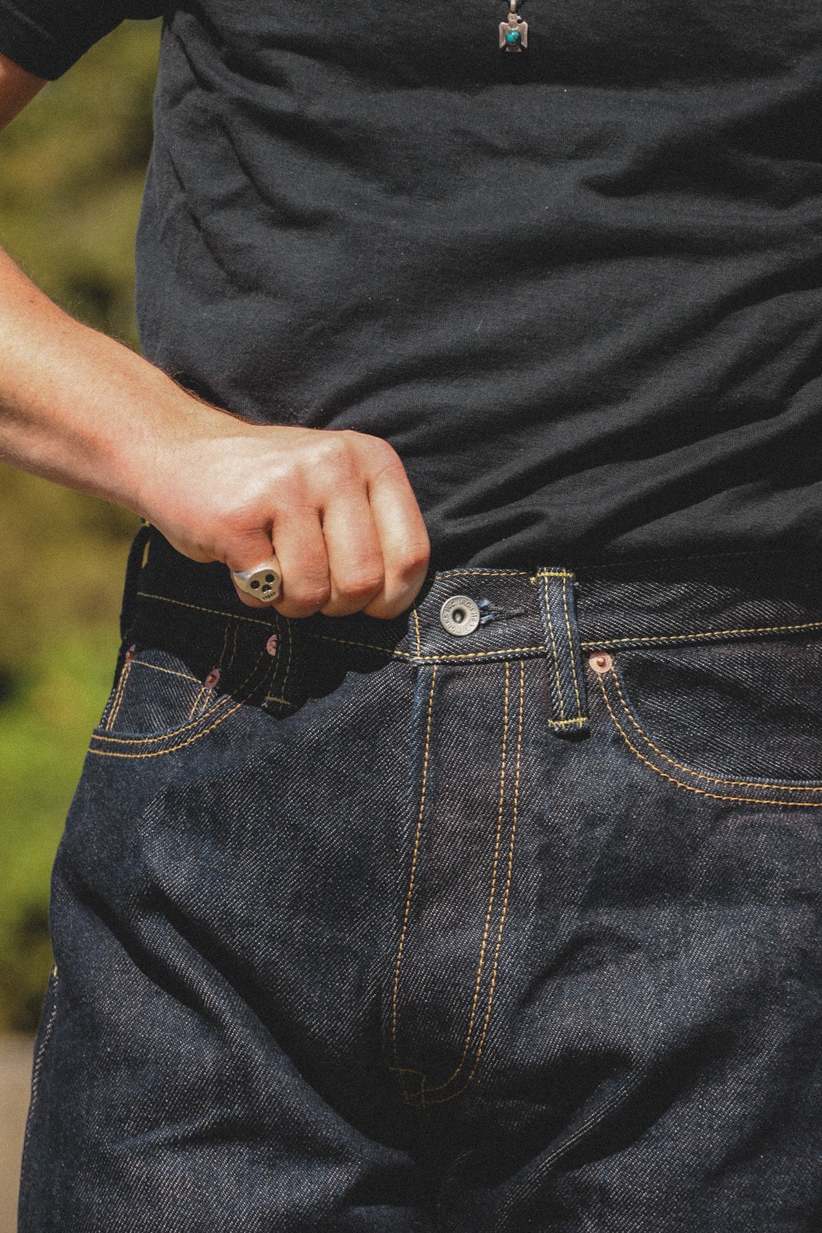 Close-up of a person wearing dark indigo denim jeans and a black t-shirt, pulling the waistband of the jeans with their hand.