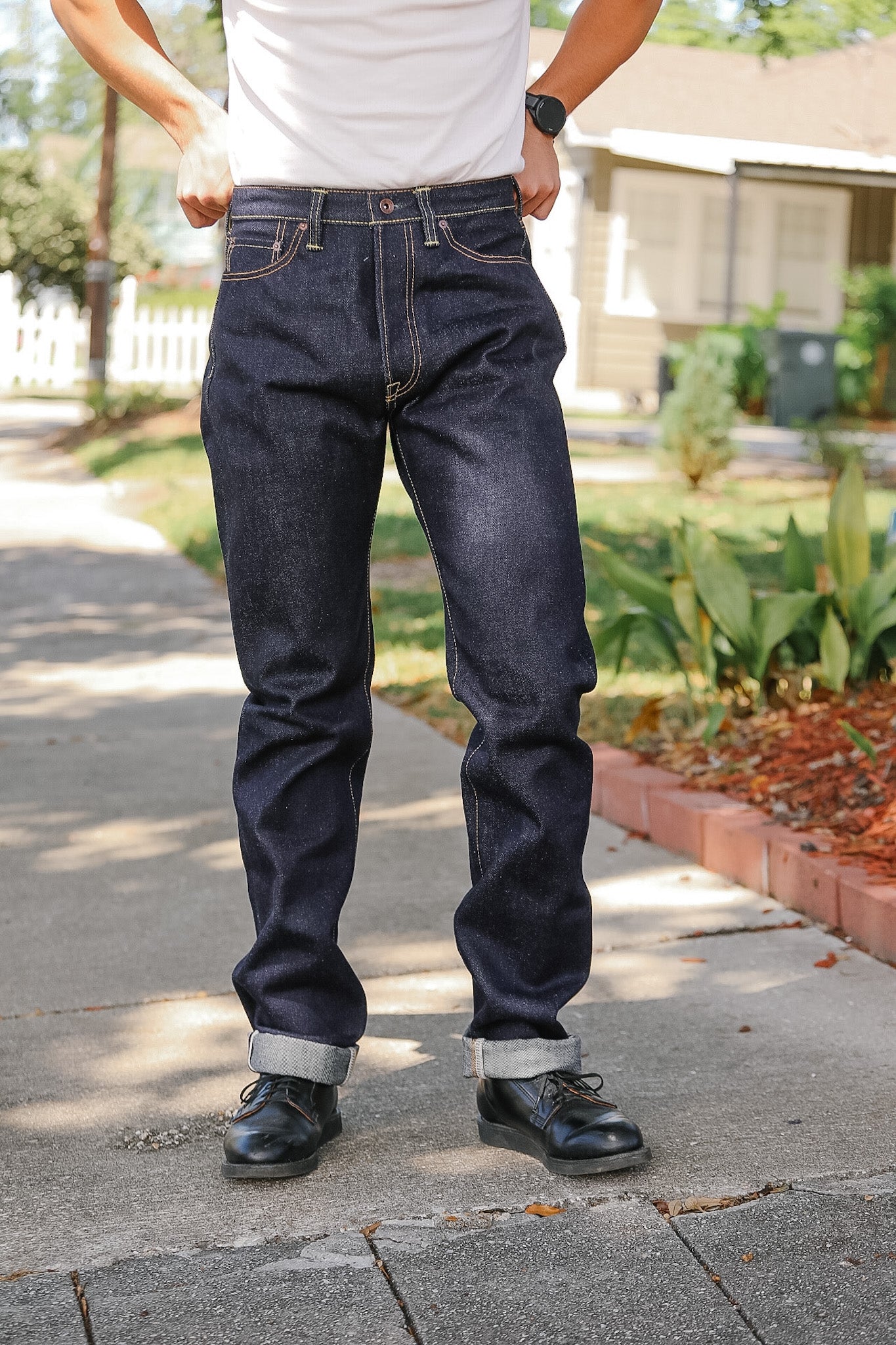 Person wearing dark blue jeans and black shoes on a sidewalk.