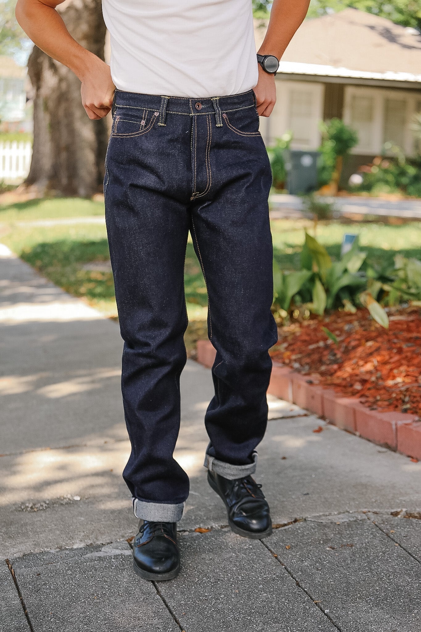 Person wearing dark blue jeans and a white shirt on a sidewalk.