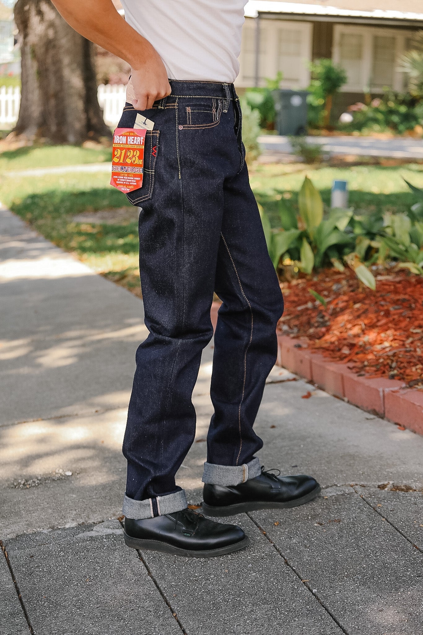 Person wearing dark blue jeans with a visible brand tag, standing on a sidewalk.