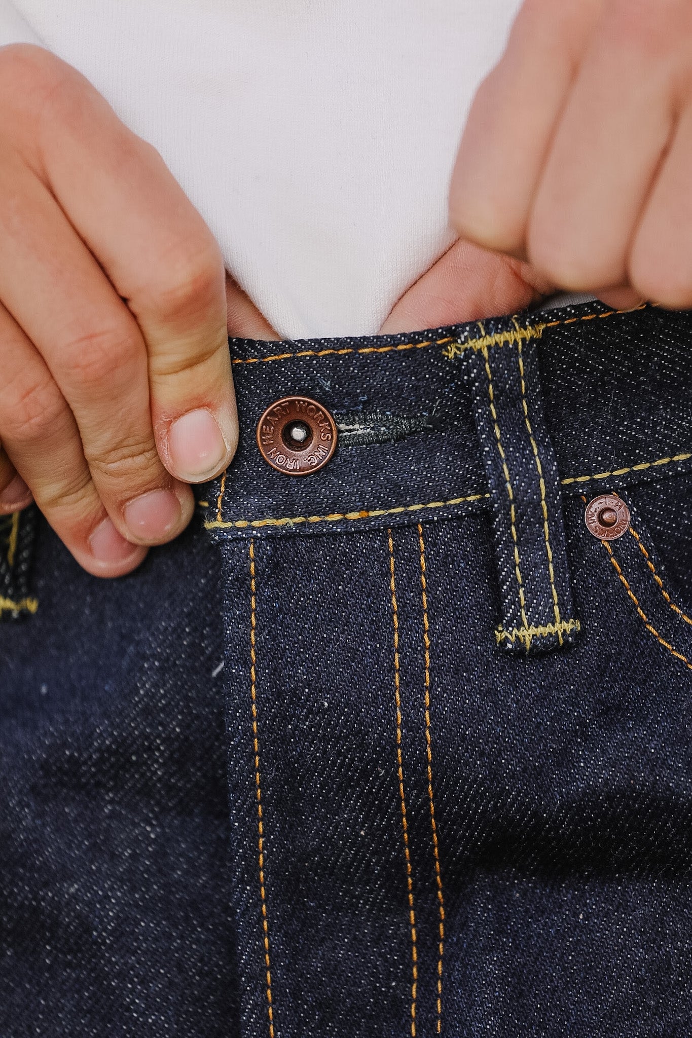 Close-up of a person adjusting a button on dark blue denim jeans.