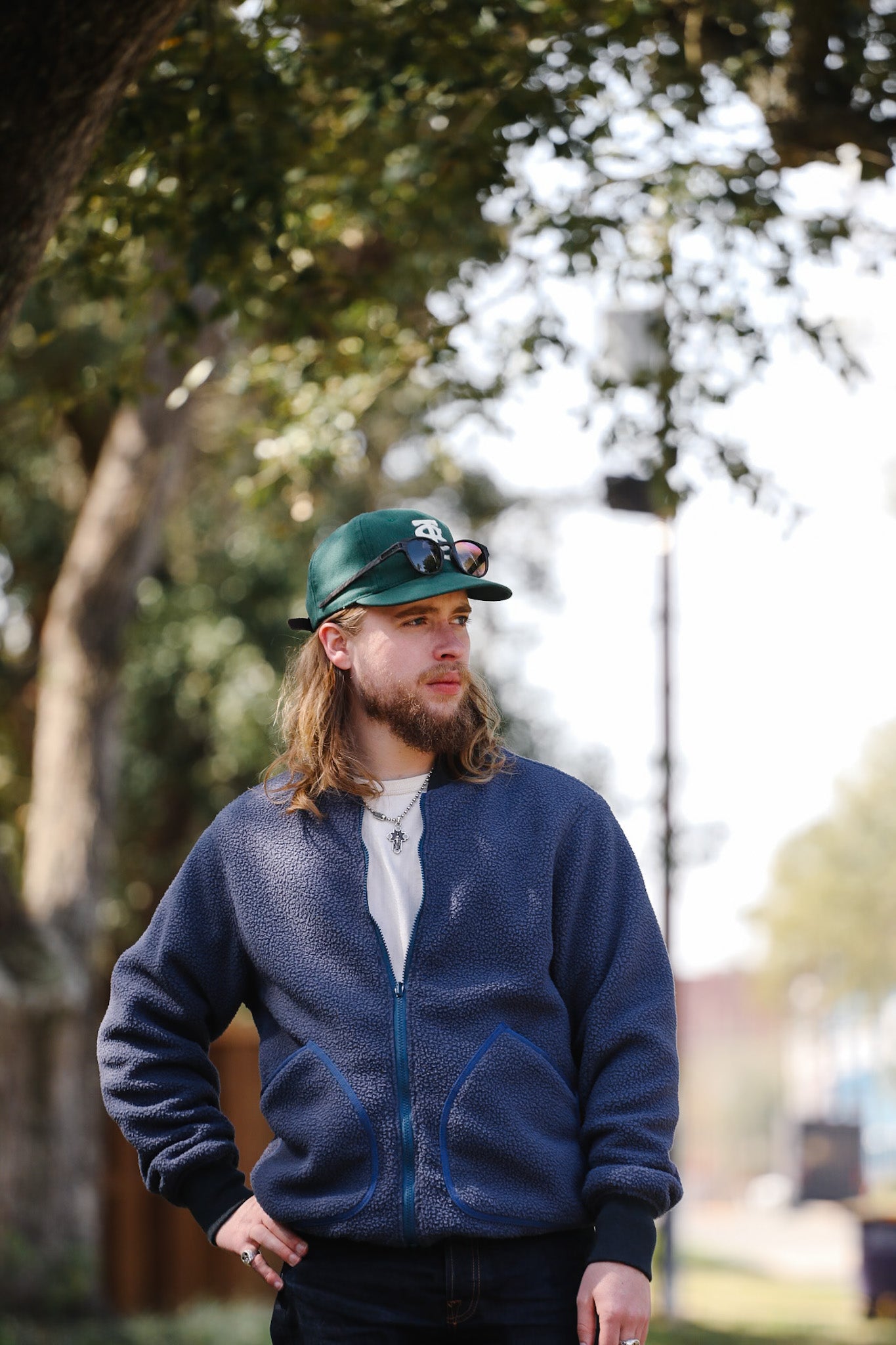 Man wearing a blue jacket and green cap outdoors with trees in the background