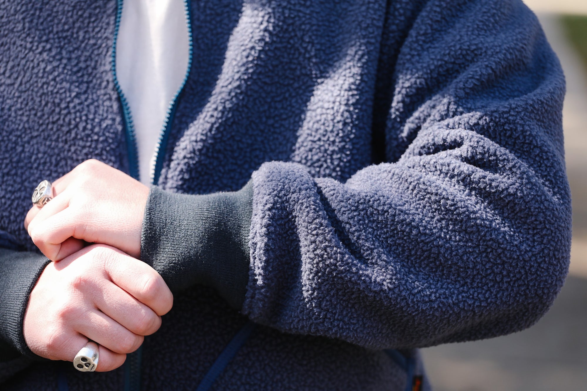 Close-up of a person wearing a blue fleece jacket with hands clasped together.