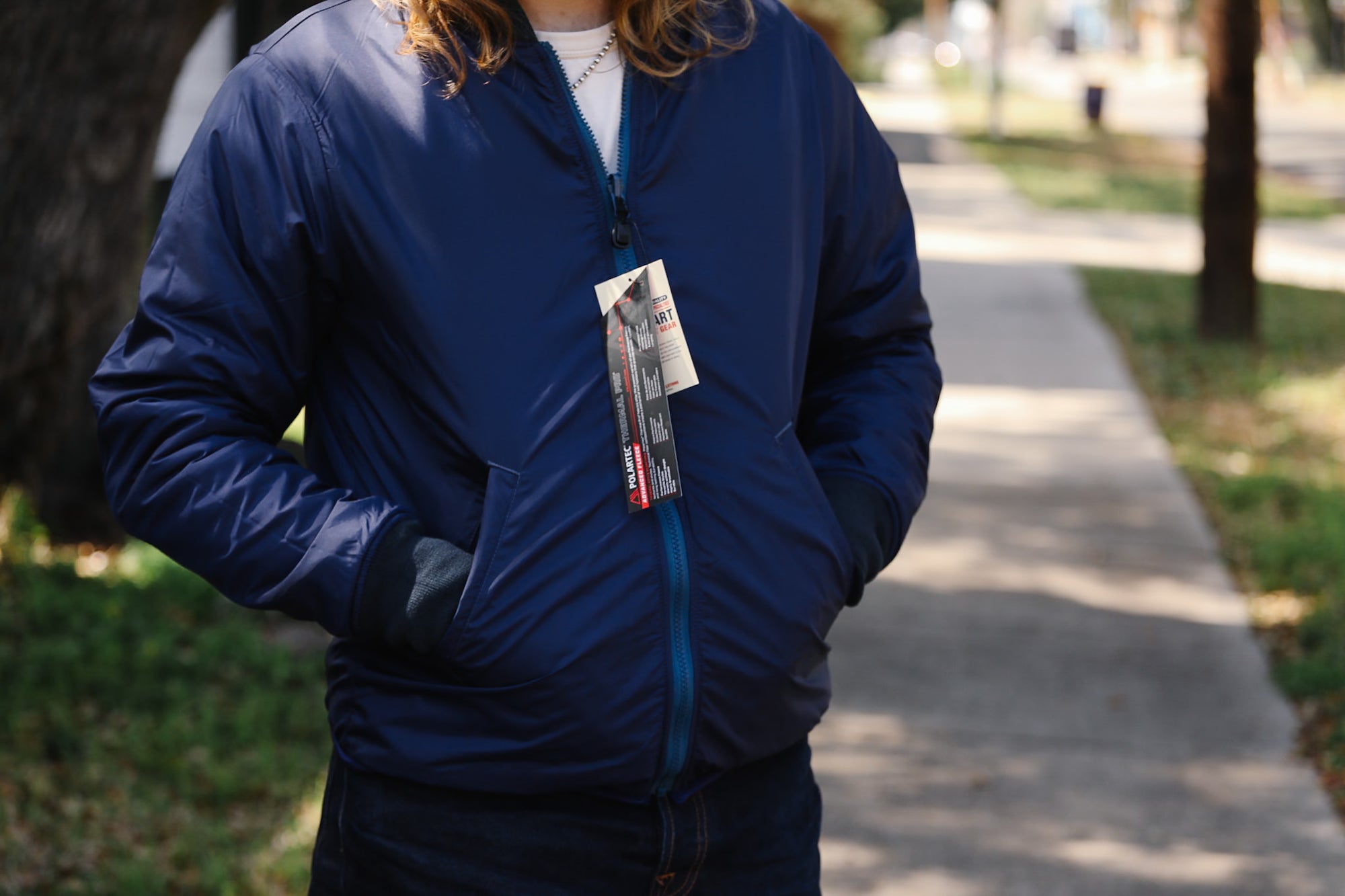 Person wearing a blue jacket with a badge on a sidewalk