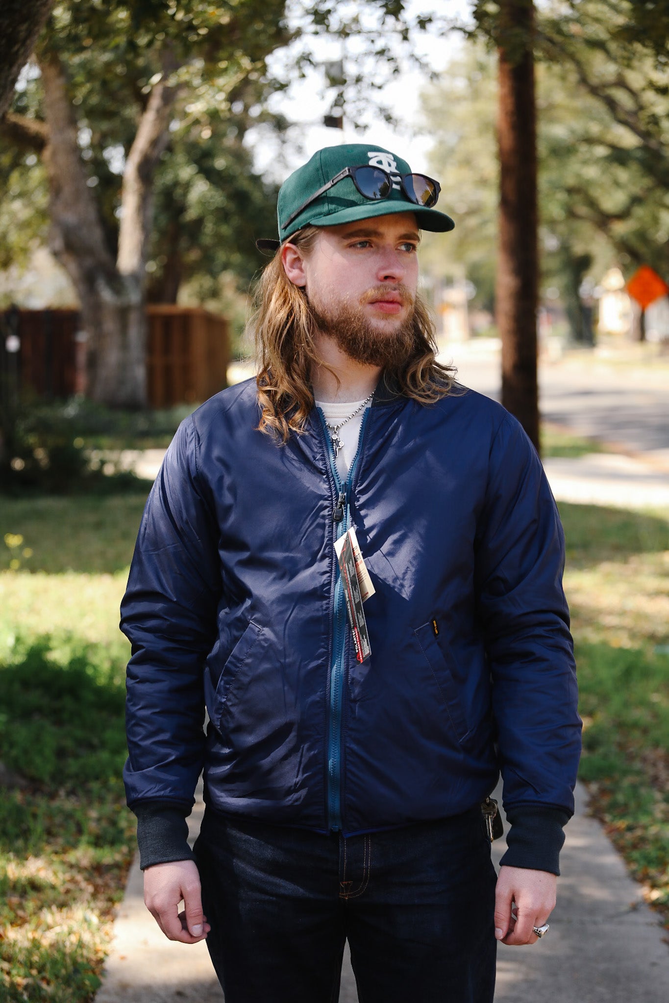 Man wearing a blue jacket and green cap outdoors on a sunny day