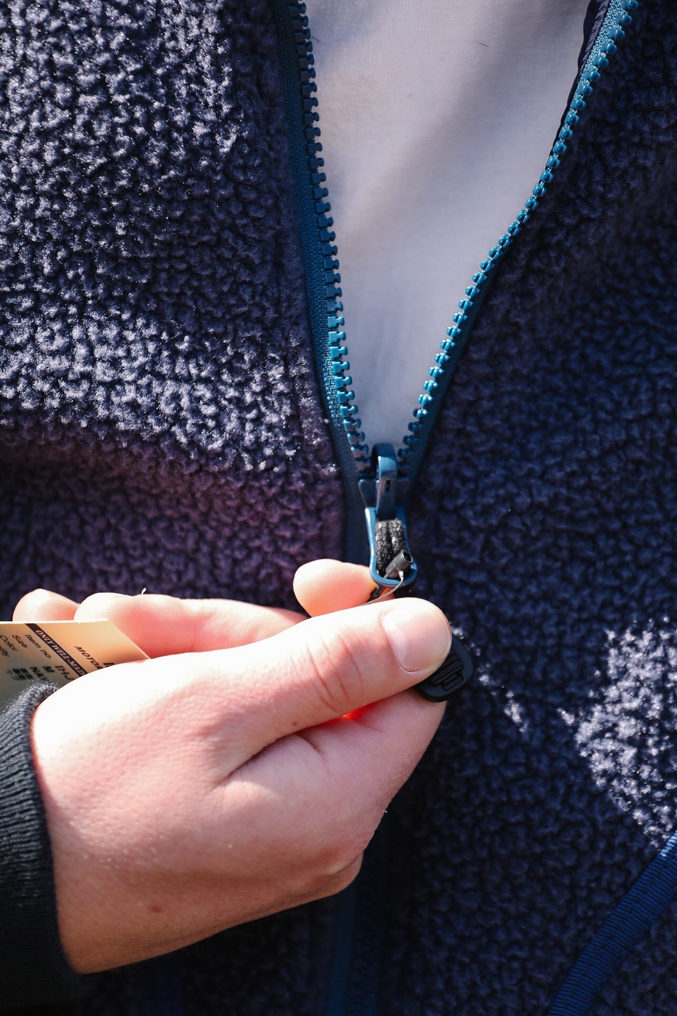 Person wearing a dark blue fleece jacket with a zipper, holding a smartphone.