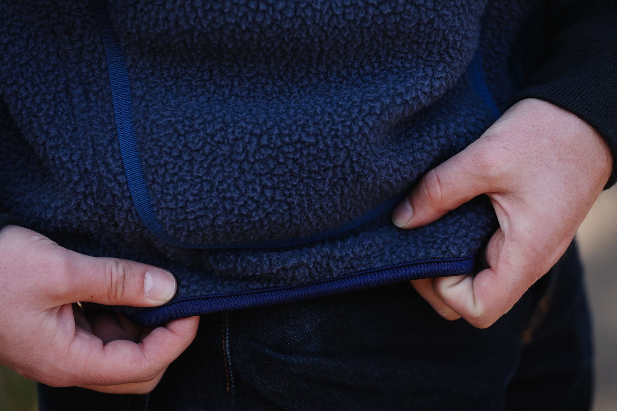 Close-up of a person adjusting the hood of a dark blue fleece jacket.