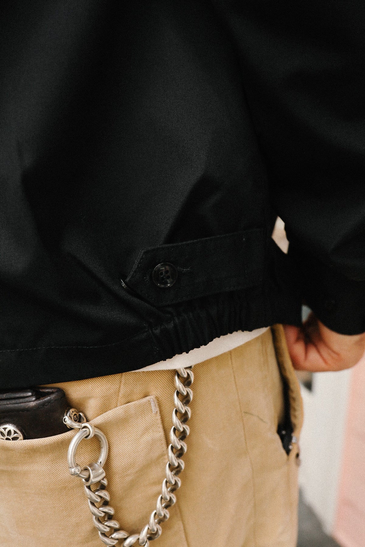 Person wearing a black jacket with a chain accessory in a pocket, blurred background