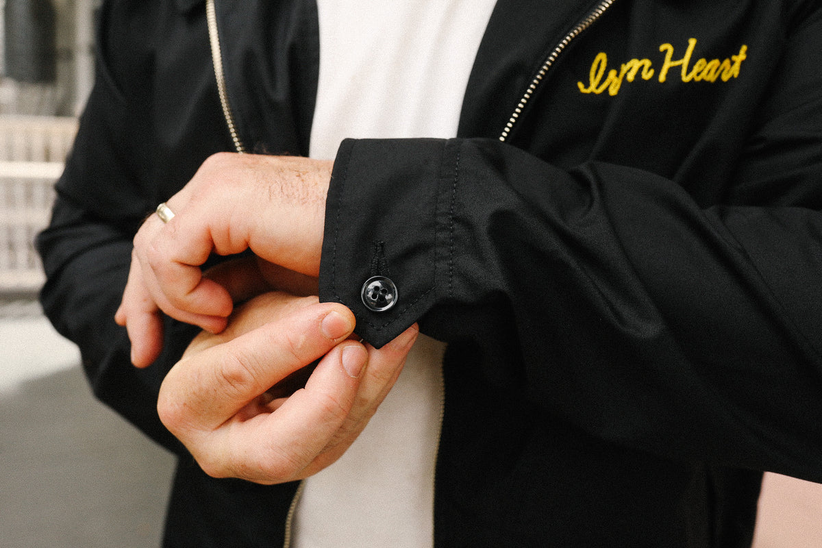 Person wearing a black jacket with 'Iron Heart' branding, adjusting the sleeve.