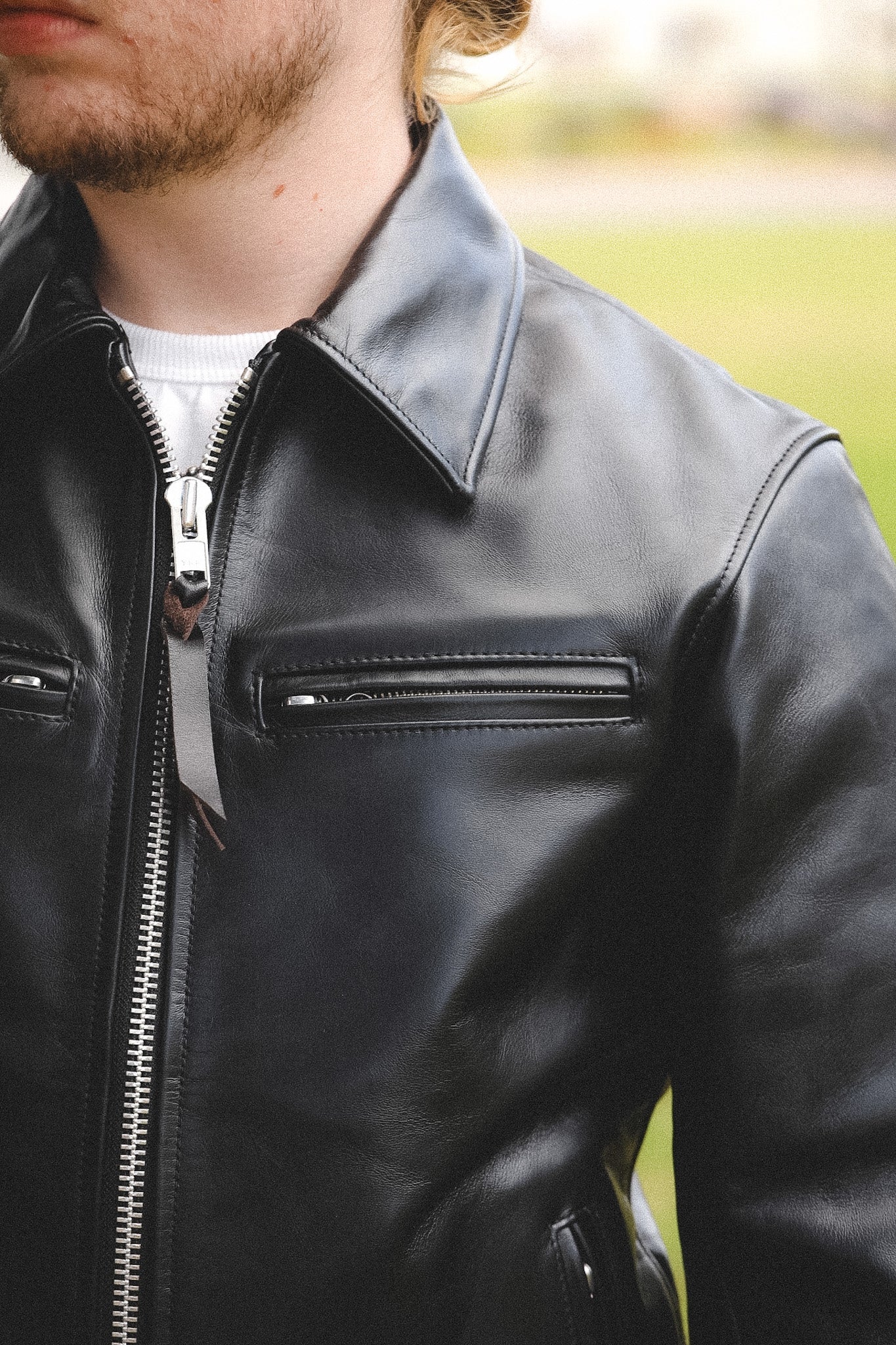 A person wearing a black horsehide rider's jacket with a collar, standing outdoors.