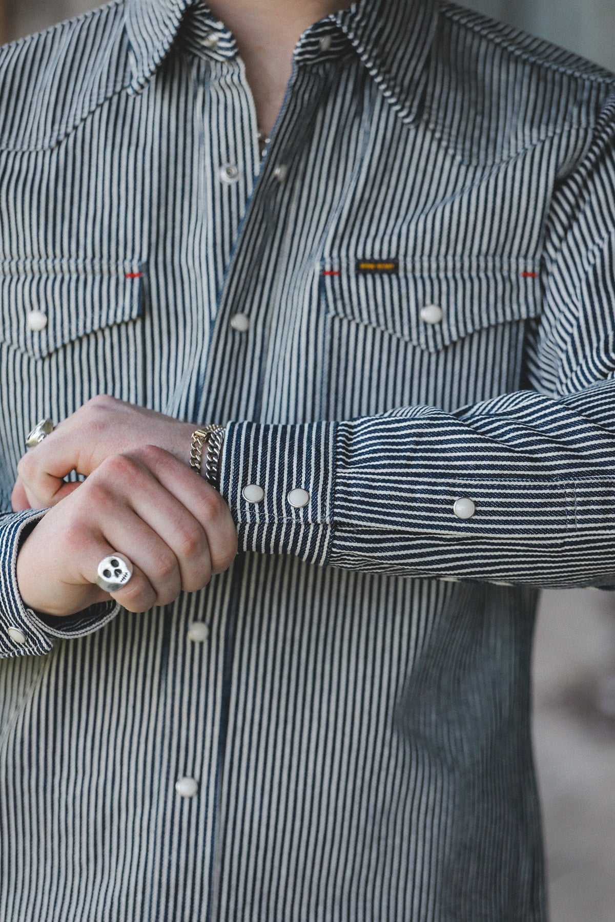 A close-up of a person wearing a black and white vertically striped button-down shirt with two chest pockets, white buttons, and a small rectangular chest label.
