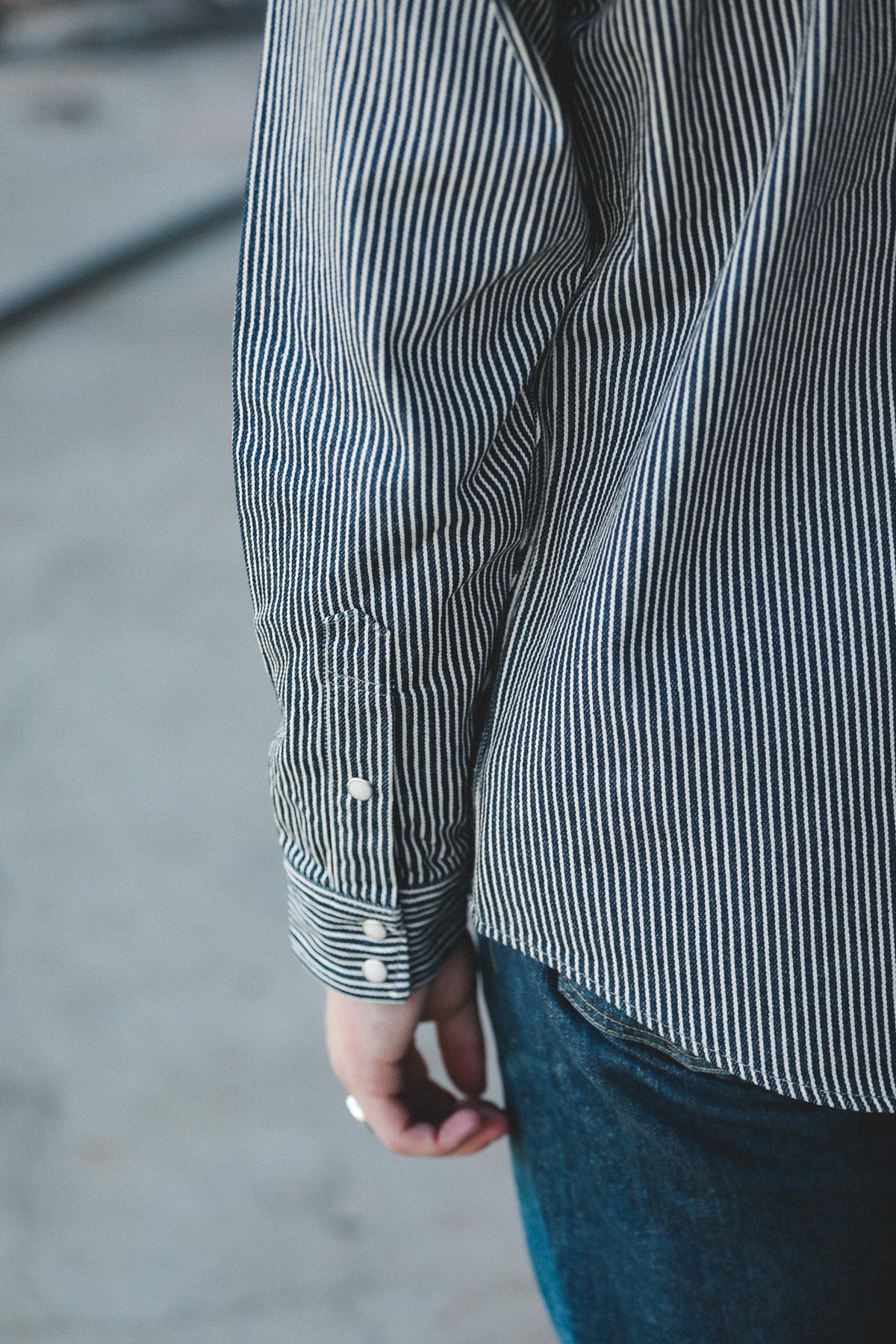 Close-up of a person wearing a navy and white vertically striped long-sleeve button-up shirt with dark blue jeans, shown from the back.
