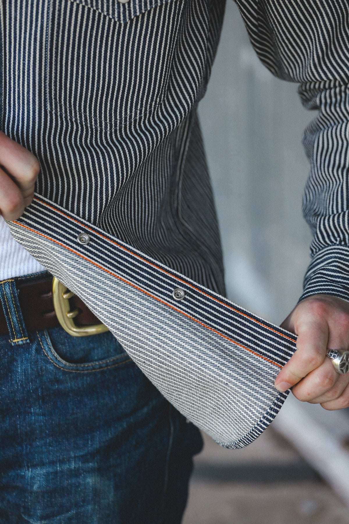 A close-up of a person wearing a black and white vertically striped button-down shirt and blue jeans, holding the shirt's sleeve cuff to show the striped fabric texture and color.