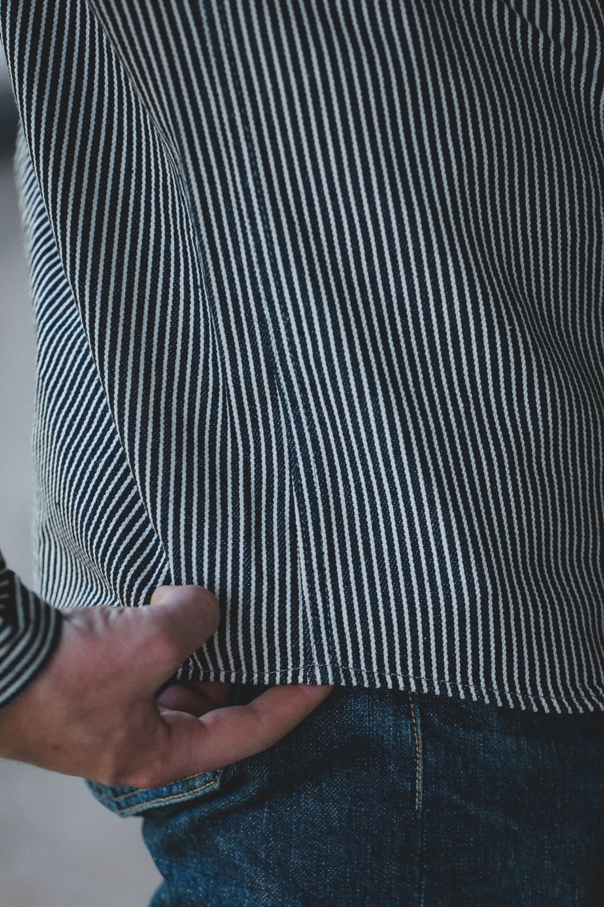 Close-up of a person wearing a dark navy and white vertically striped shirt, with a hand pulling the hem slightly to show the fabric drape, paired with blue jeans.