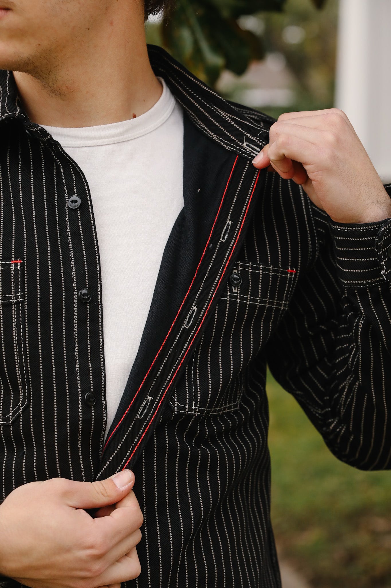 Person wearing a black pinstripe jacket with a white shirt, outdoors.