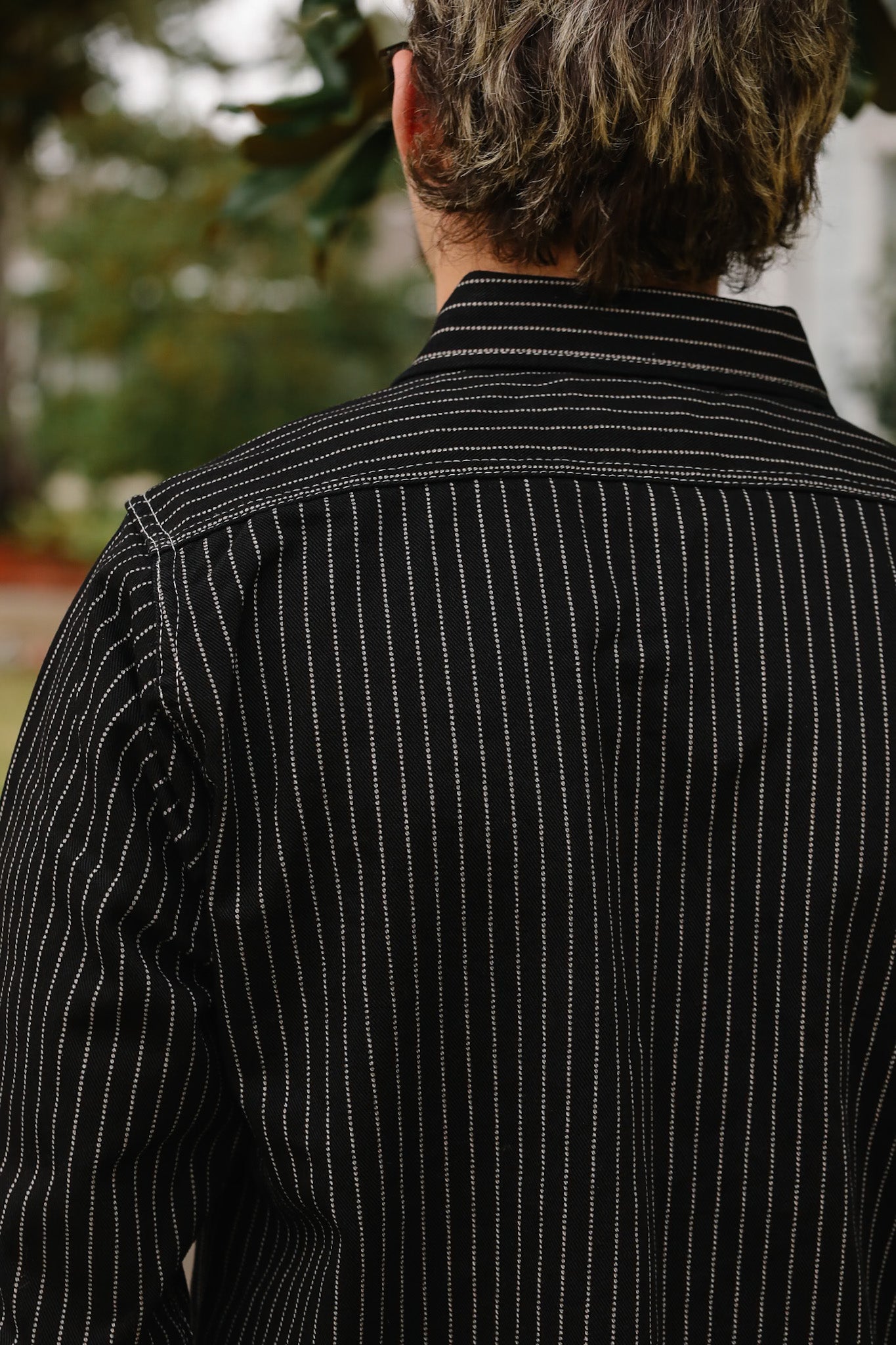 Person wearing a black pinstripe shirt with a blurred outdoor background
