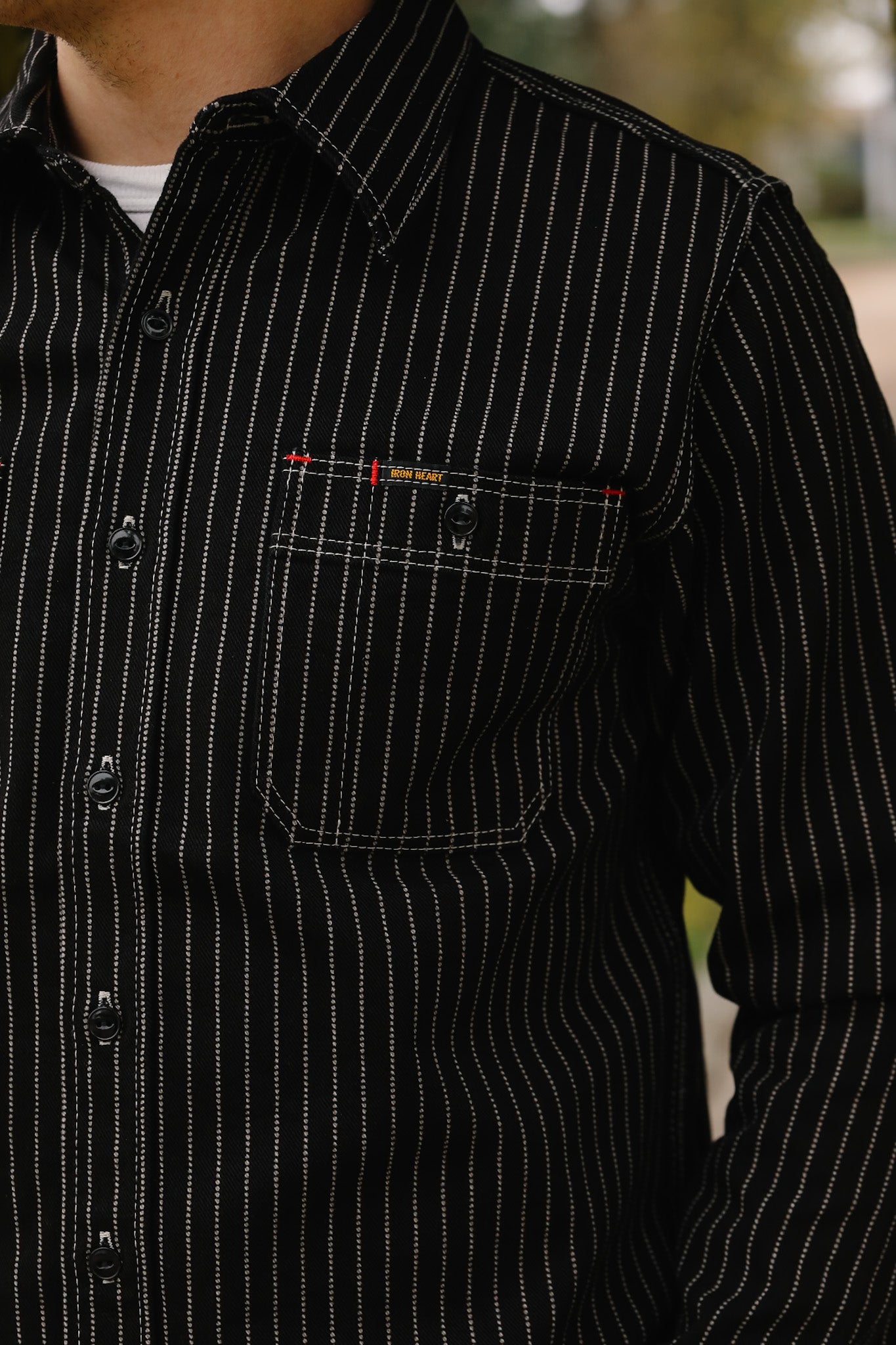 Close-up of a person wearing a black pinstripe shirt with a brand logo on the chest pocket.