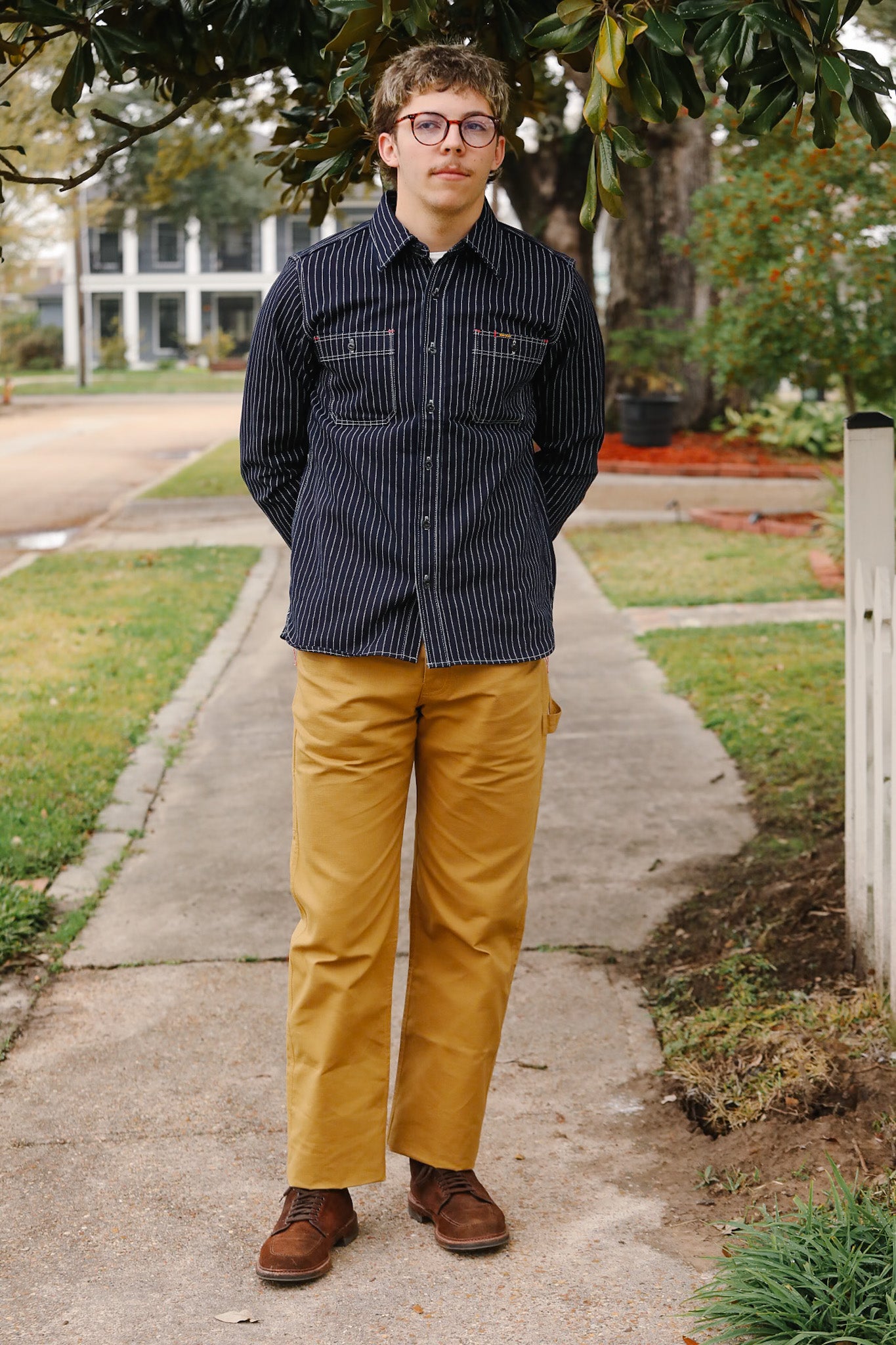 Man standing on a sidewalk wearing a dark shirt and yellow pants.