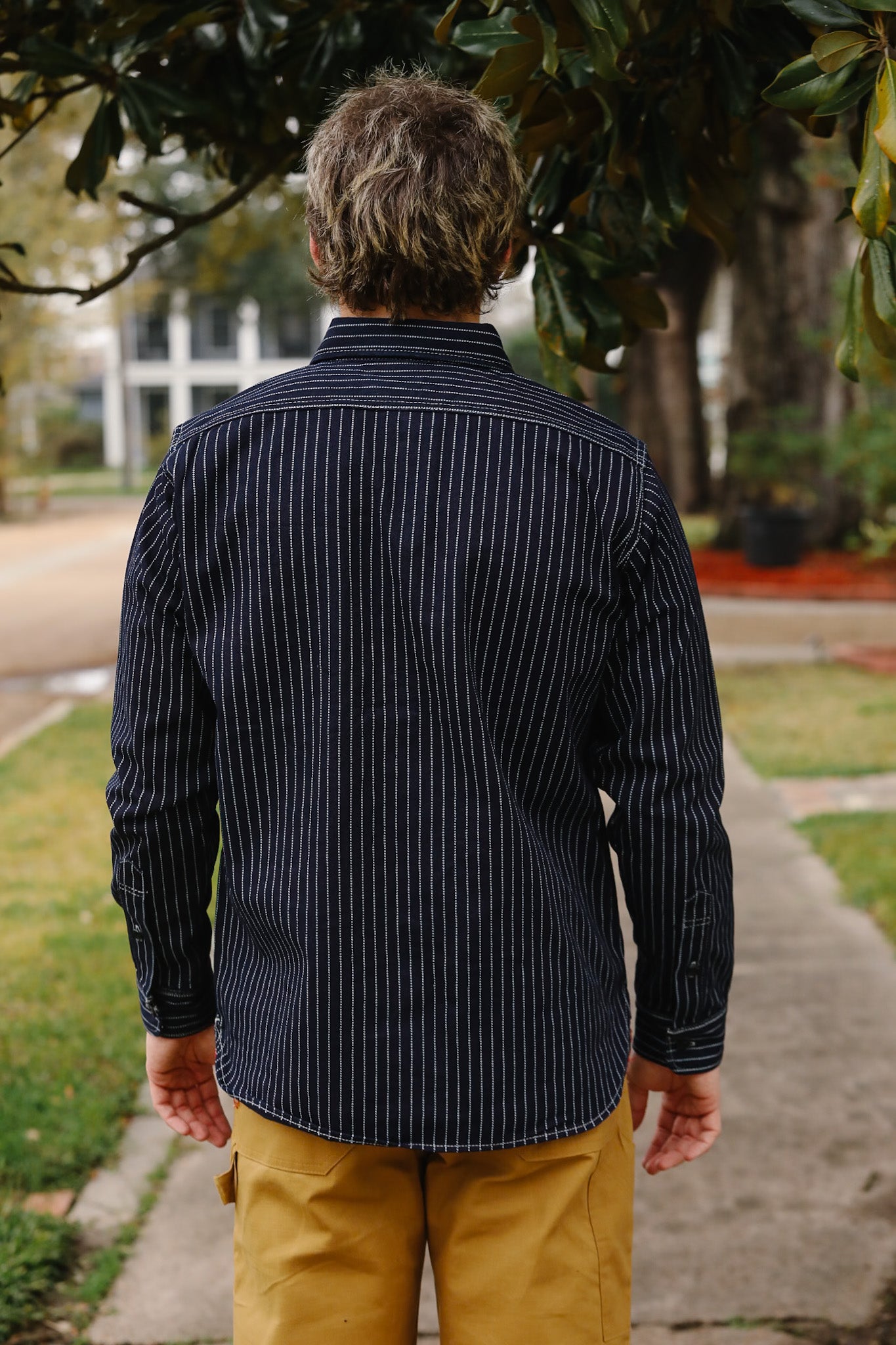 Person wearing a black pinstripe shirt and yellow pants standing outdoors.