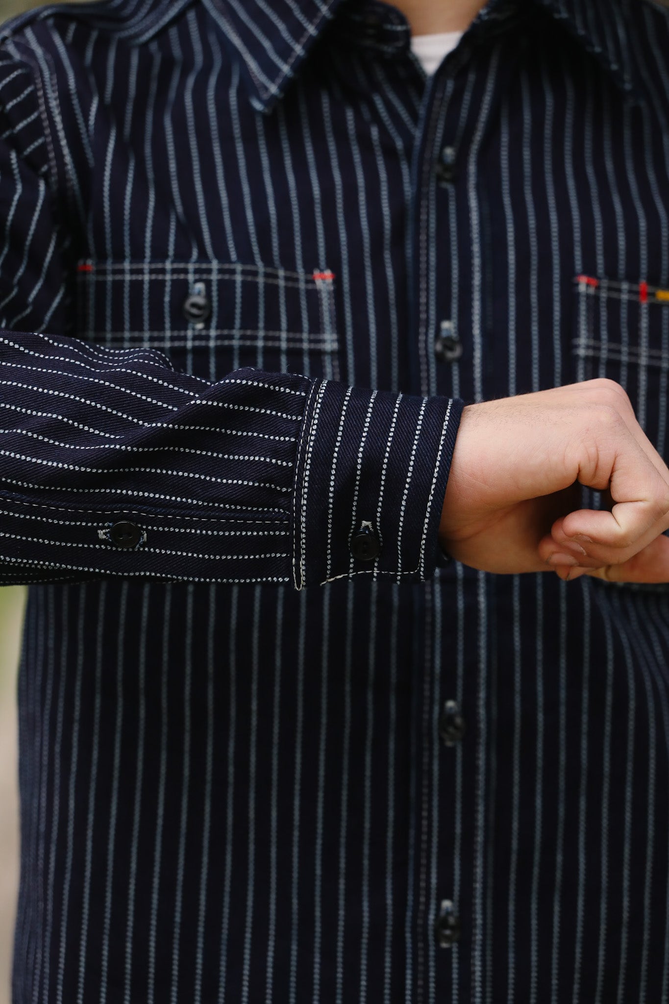 Close-up of a person wearing a dark blue striped shirt with a focus on the sleeve and hand.