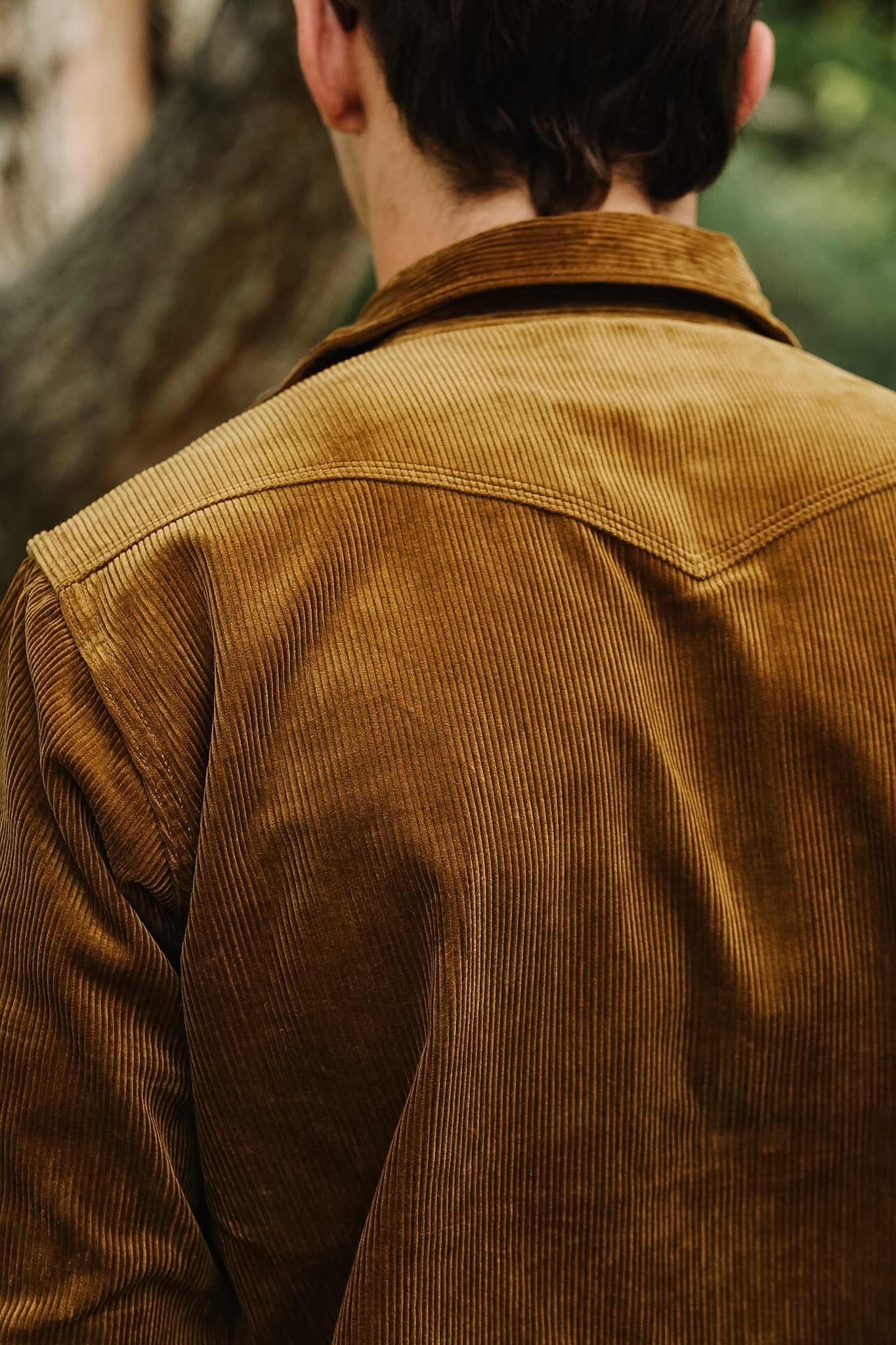Close-up of a brown corduroy shirt and blue jeans with a blurred background
